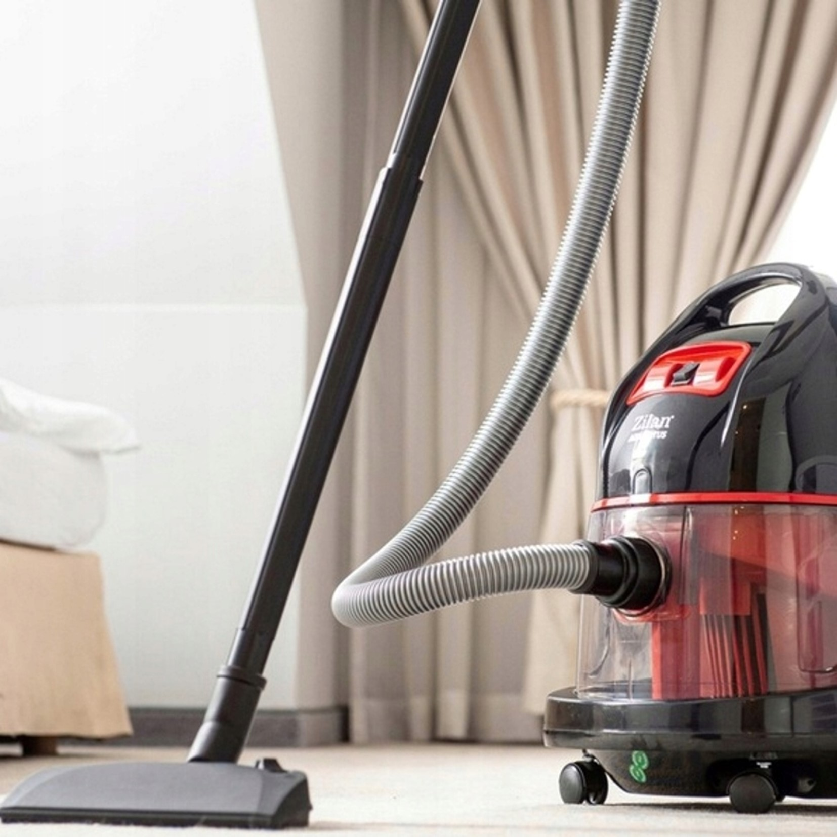 Czarny odkurzacz z czerwonymi akcentami i wężem na jasnym dywanie.