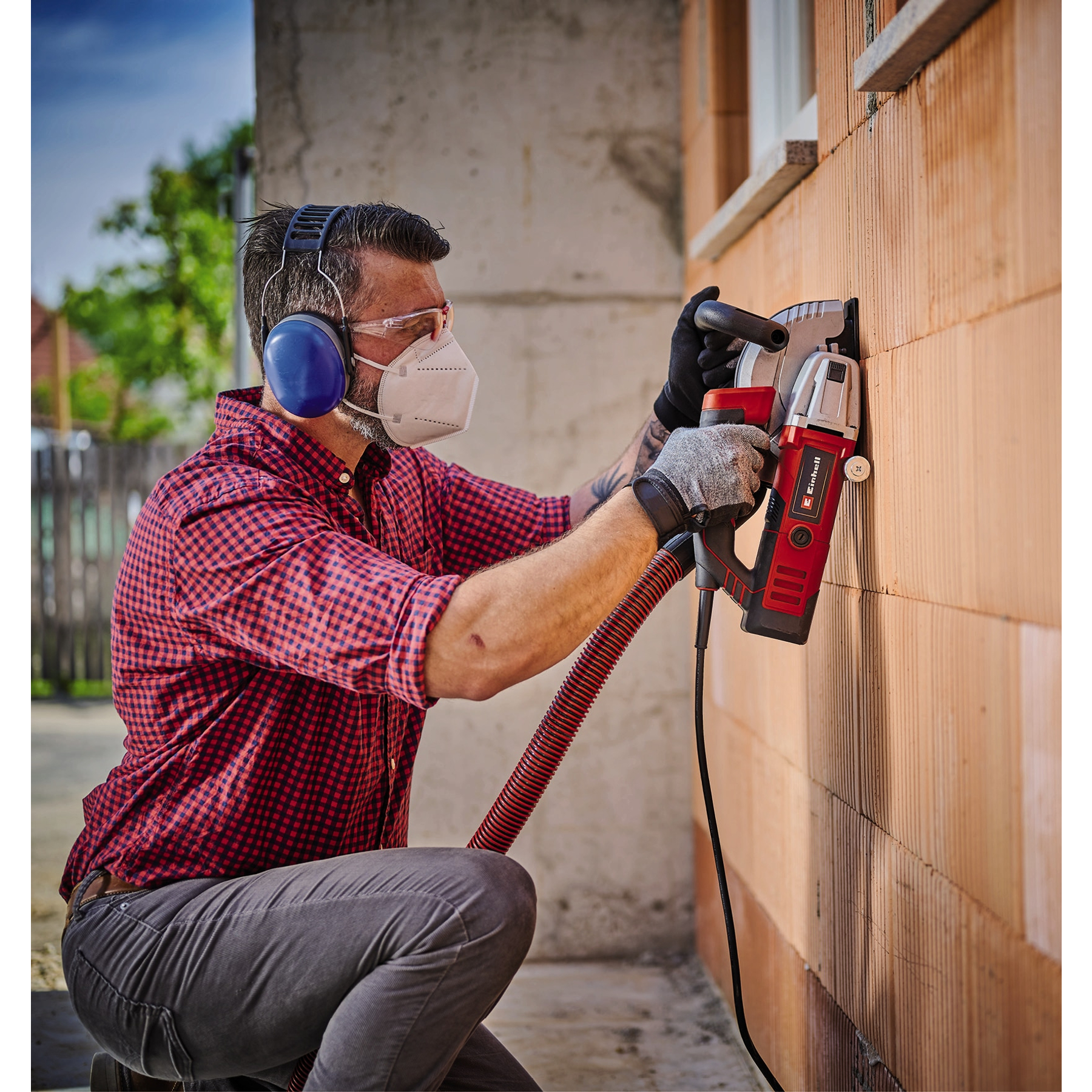 Homme avec équipement de sécurité coupe mur avec outil électrique.