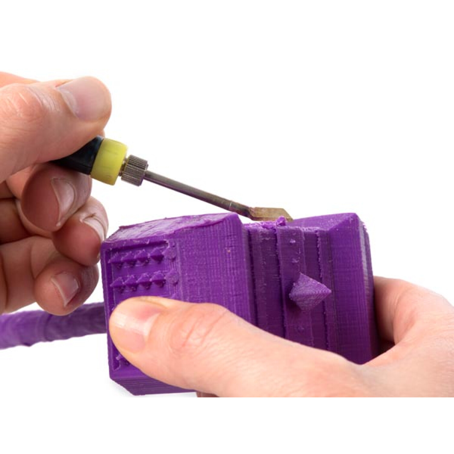 Mani che lavorano su un oggetto stampato in 3D viola con uno strumento.