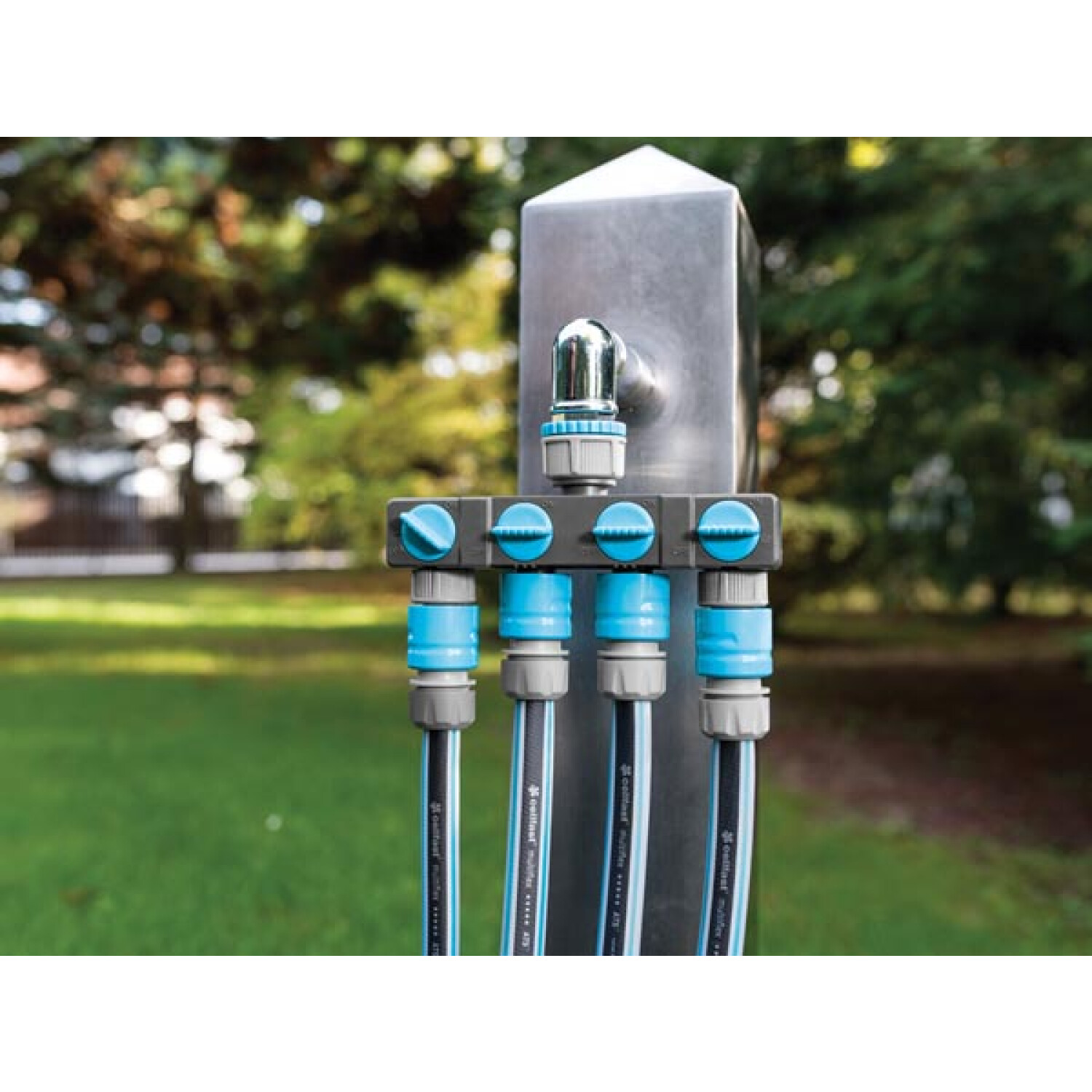 Ein Wasserkran mit vier Anschlüssen und verbundenen Schläuchen im Garten.