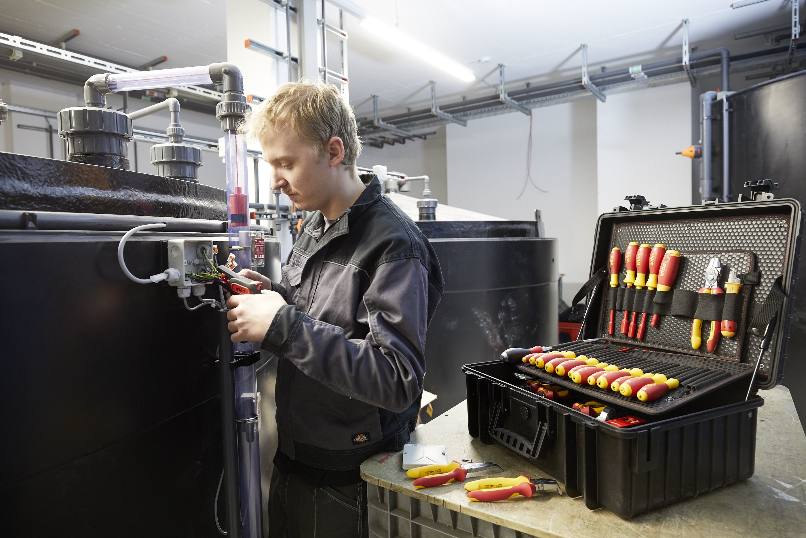 Ein Mann arbeitet an elektrischen Leitungen neben einem schwarzen Tank.