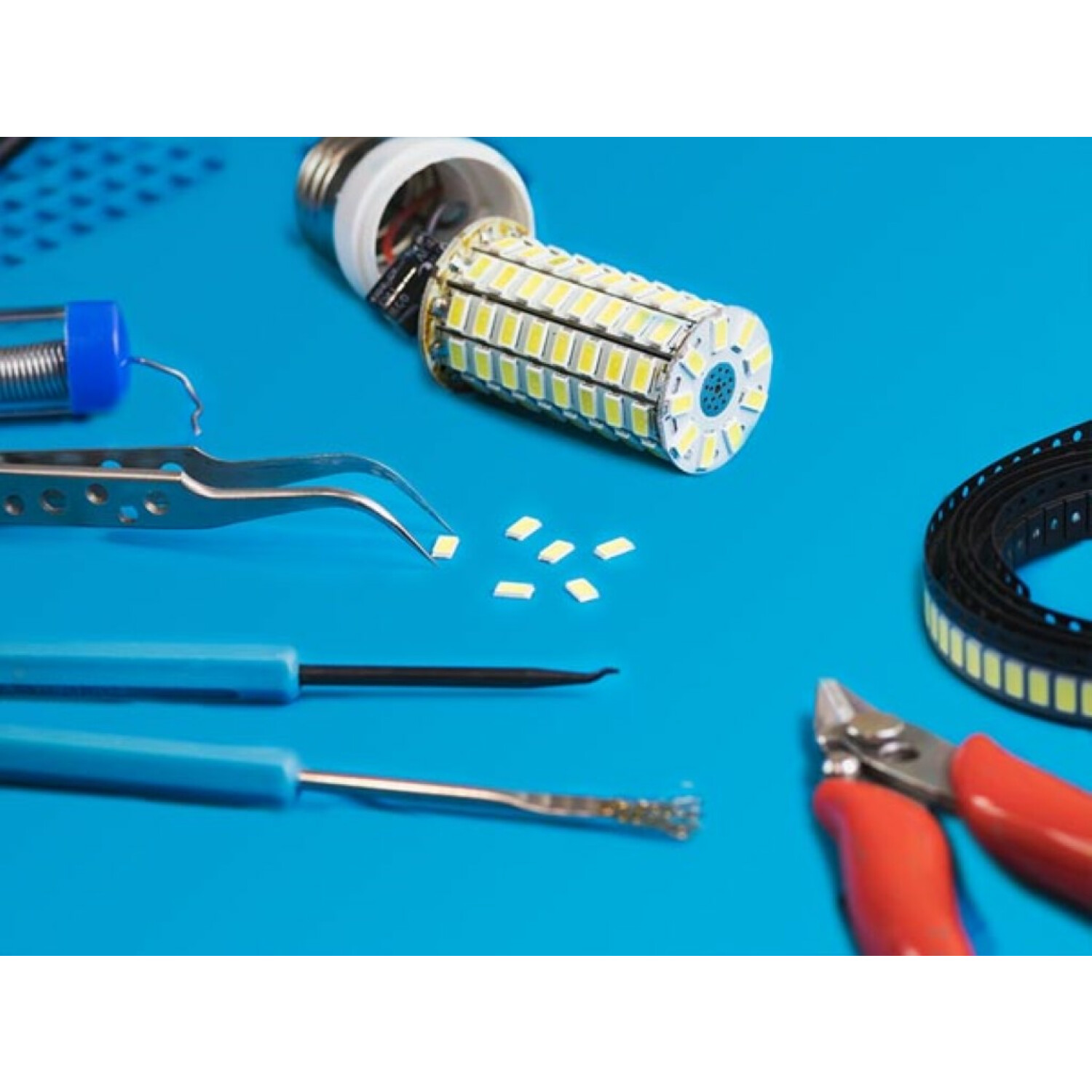 LED-Glühbirne mit Werkzeugen, Lötmittel, Pinzette, Schere und Kleinteilen auf blauem Untergrund.