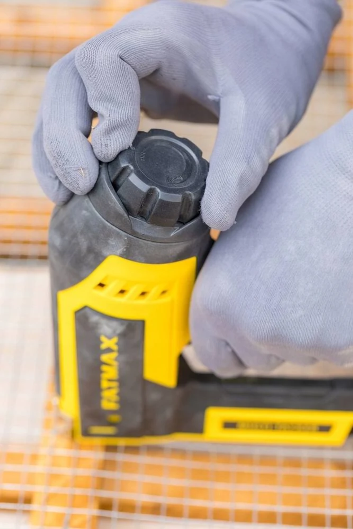 Mani guantate di grigio regolano una manopola nera su un attrezzo giallo e nero.