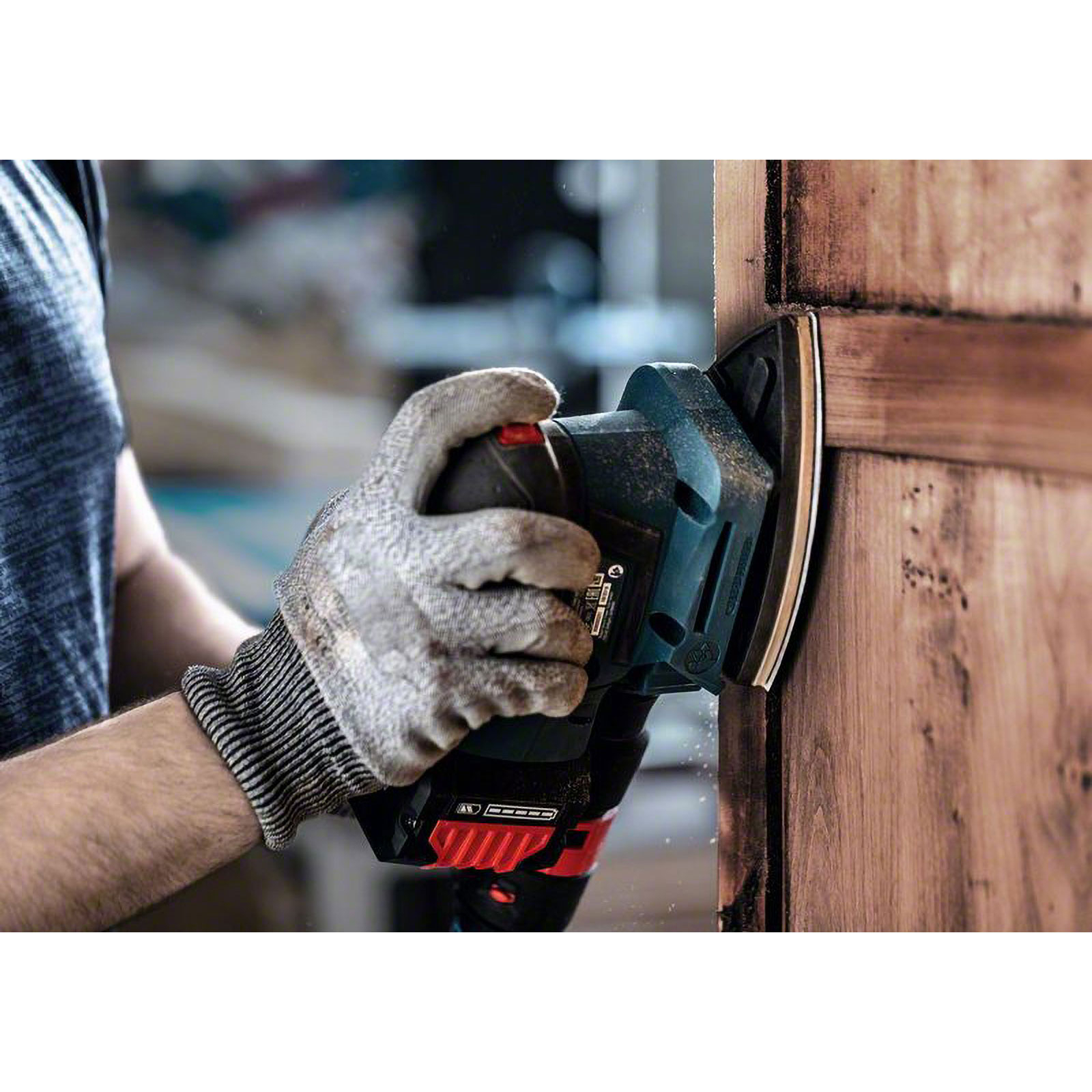 Ein Mann schleift Holz mit einem Dreieckschleifer, Staub wirbelt auf.