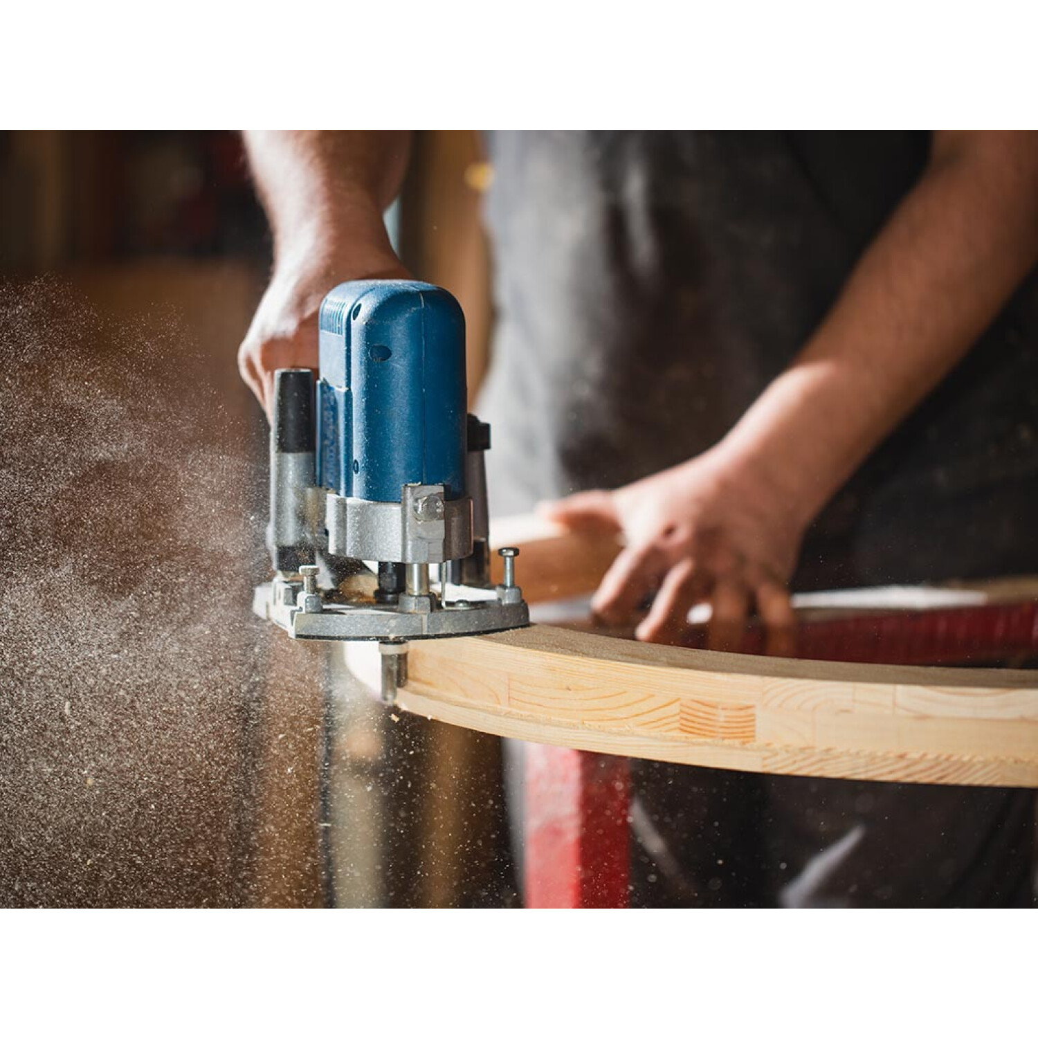 Ein Handwerker benutzt einen blauen Router, um Holz zu formen. Holzstaub fliegt.