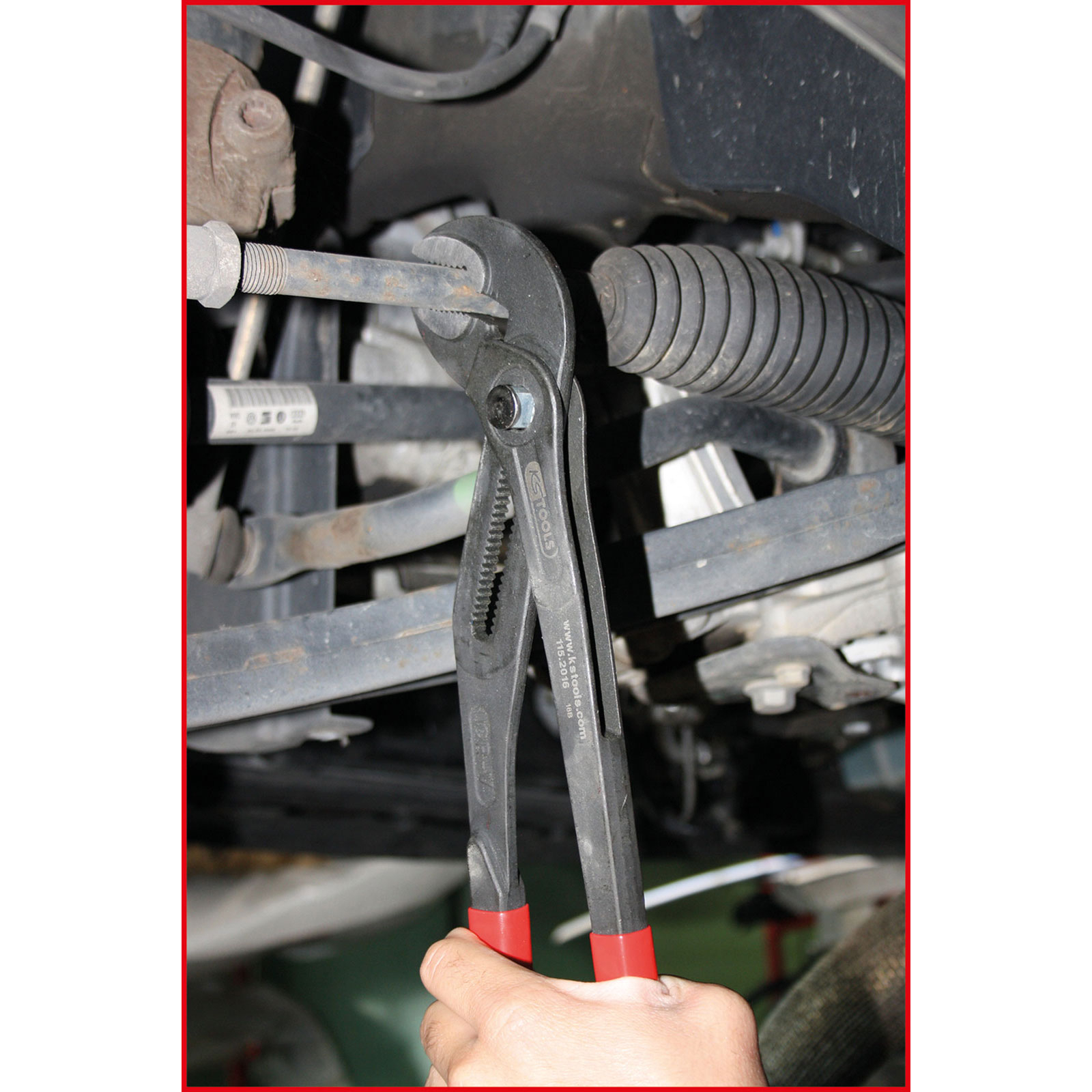 Eine Hand hält eine Zange, die eine Schraube am Auto-Fahrwerk greift.