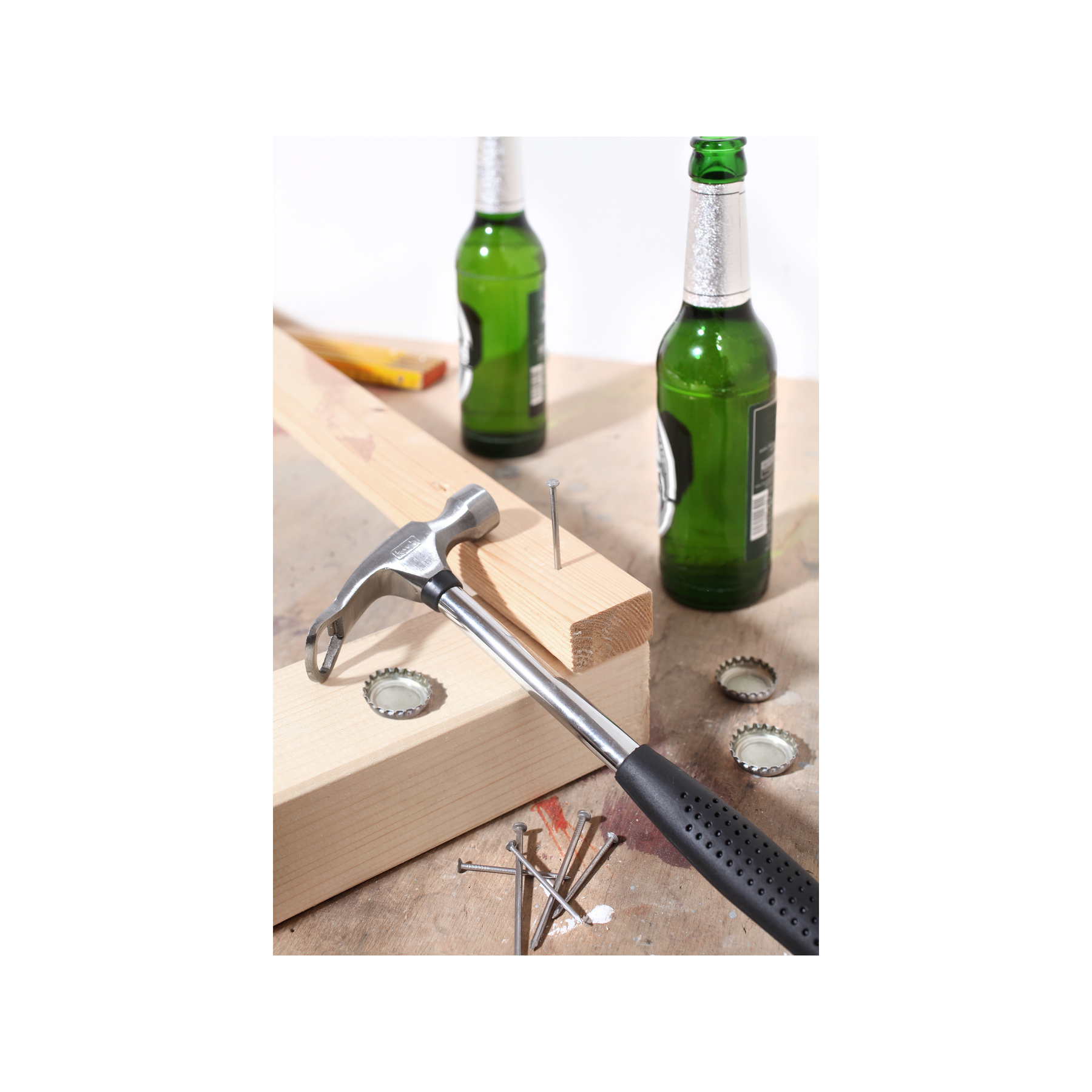 Hammer, Nagel und Holz auf einem Tisch mit Bierflaschen und Kappen.