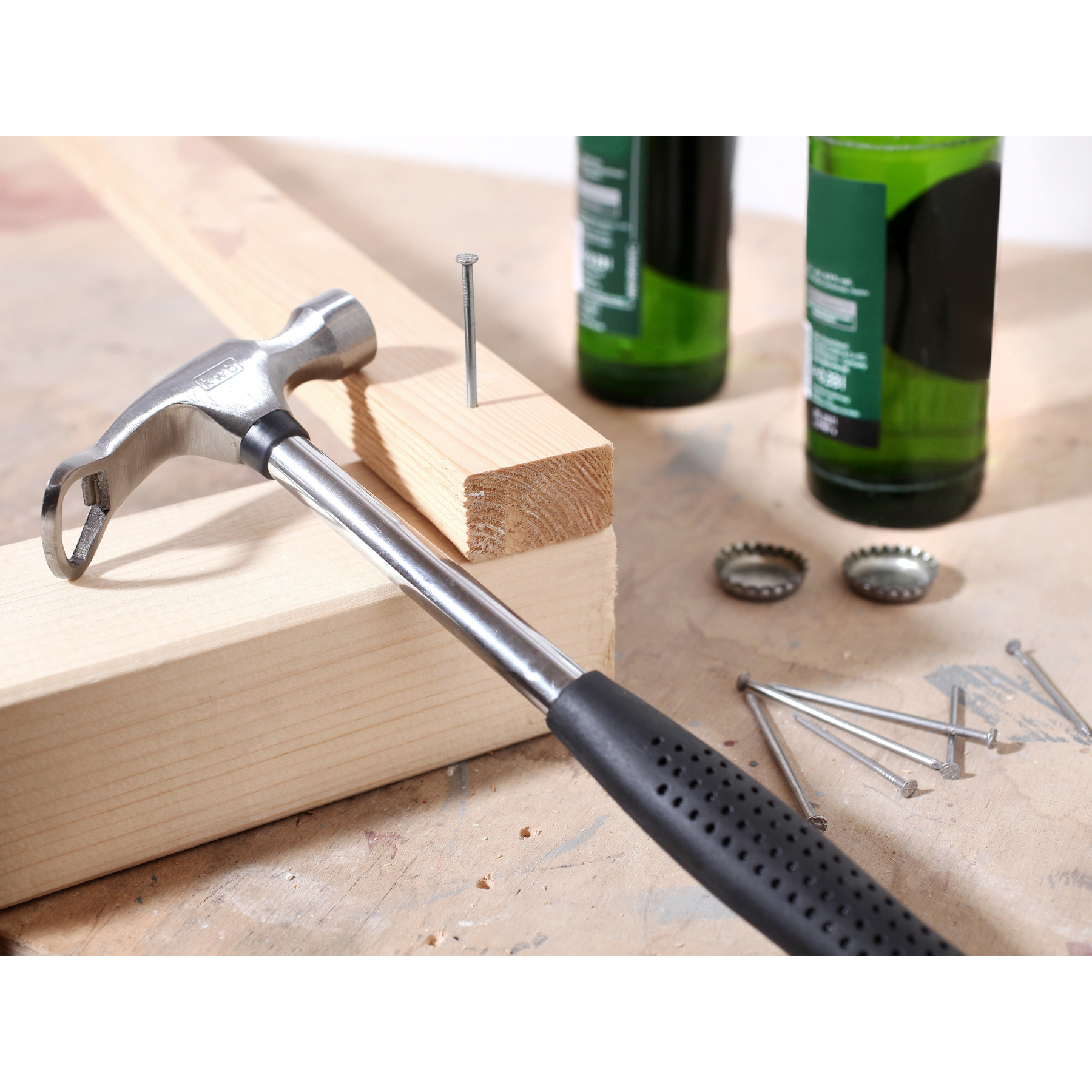 Ein Hammer liegt auf Holz. Nägel, Flaschen und Kappen sind in der Nähe.