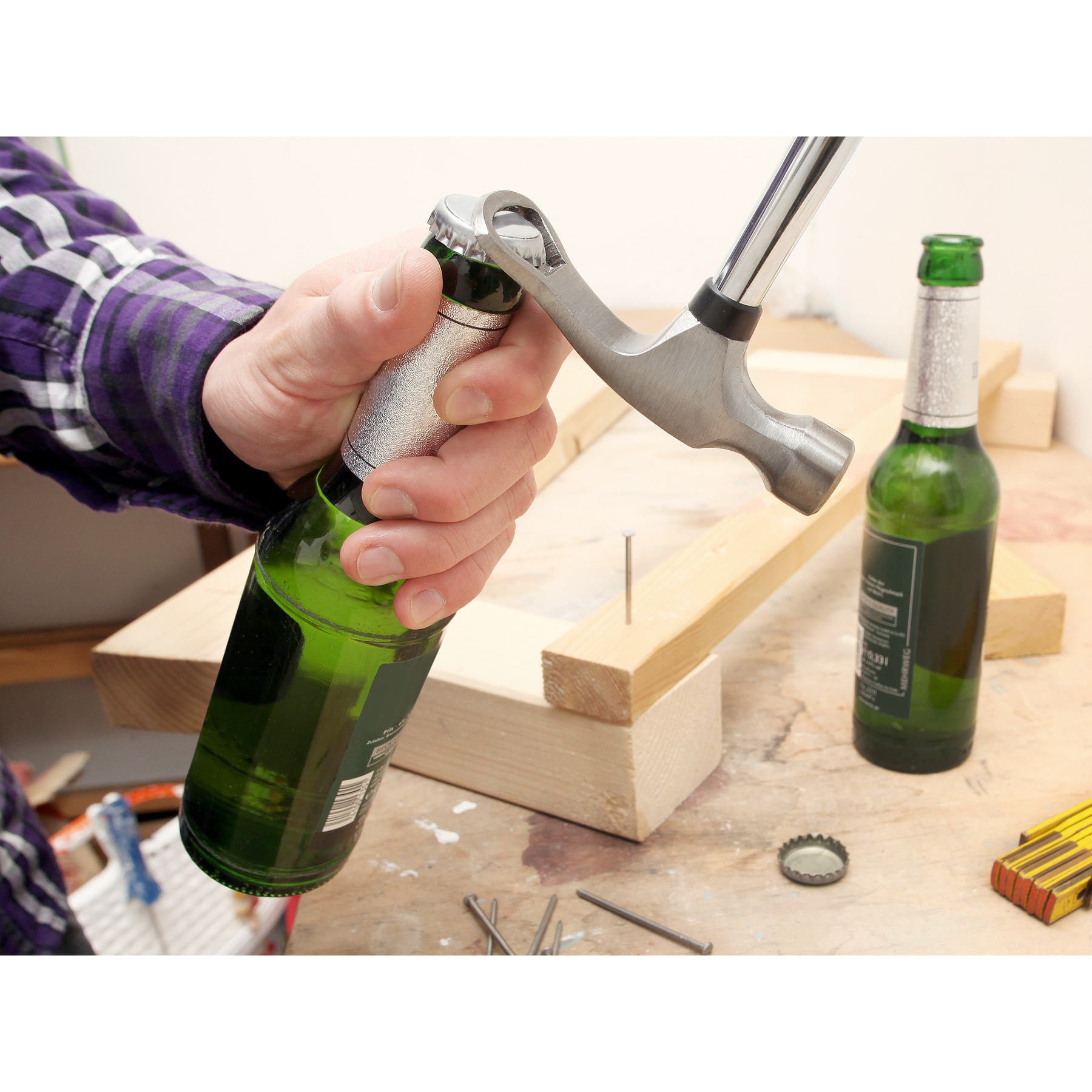 Mann öffnet Bierflasche mit einem Hammer-Flaschenöffner auf Holz.