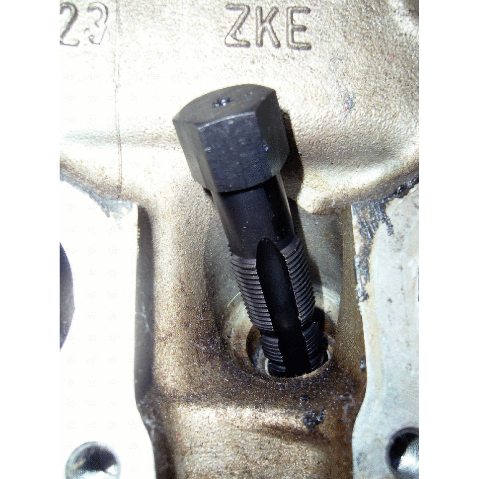 Ein schwarzes Werkzeug mit Rillen steckt in einem metallischen Bauteil.