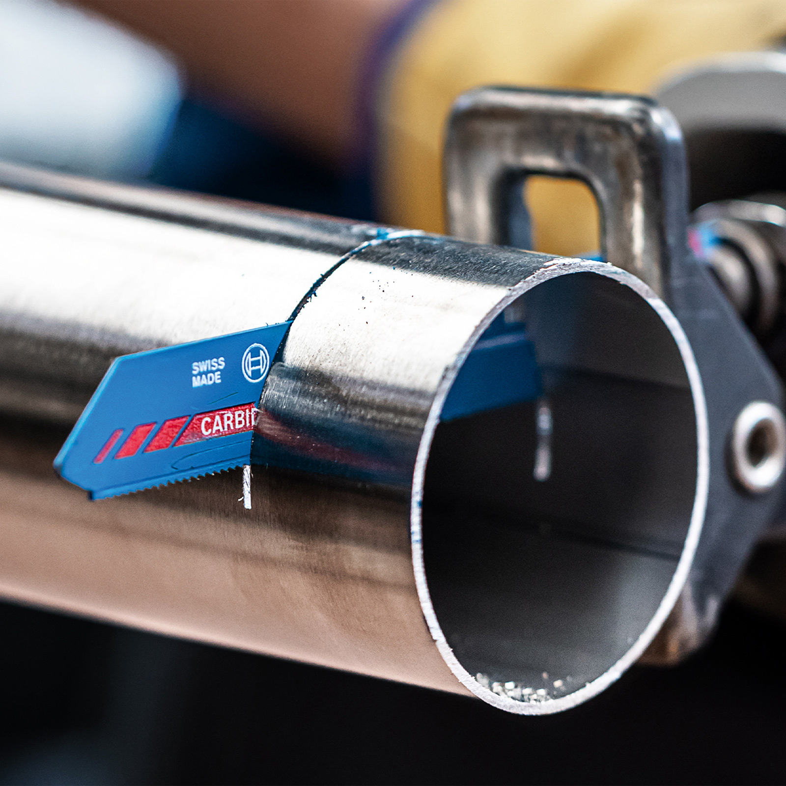 Una lama di sega blu "Swiss Made" taglia un tubo metallico.