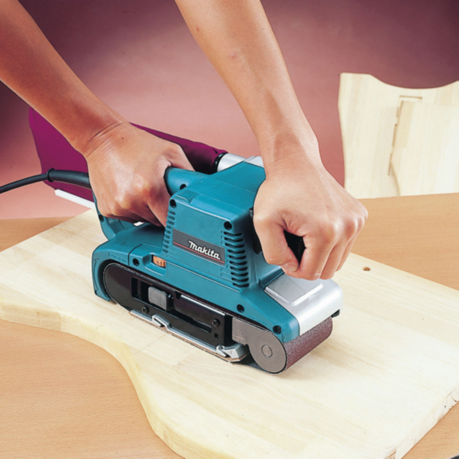 Una persona leviga legno con una levigatrice a nastro blu e argento.
