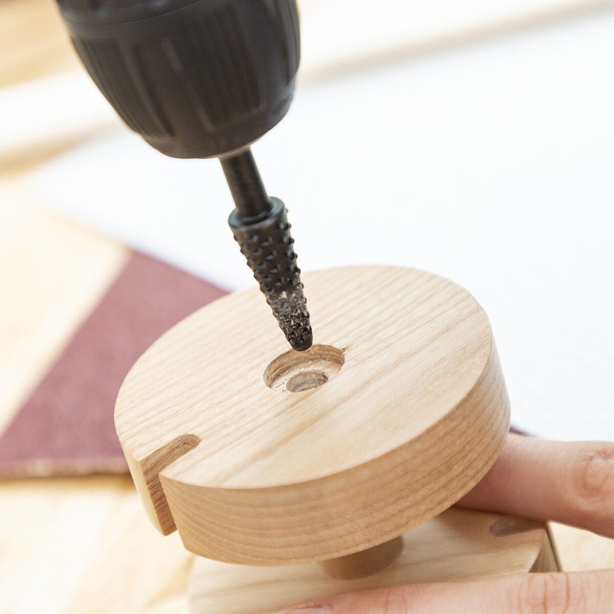 Una punta di trapano allarga un foro in un pezzo di legno. Polvere visibile.
