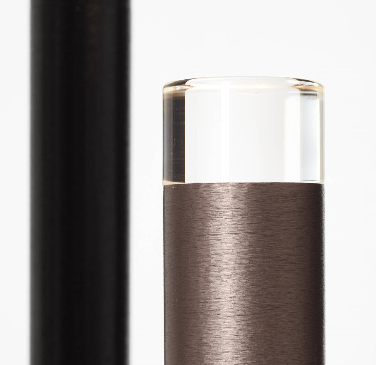 Ein schwarzer Stab links, ein zylindrisches Objekt aus Metall und Glas rechts.