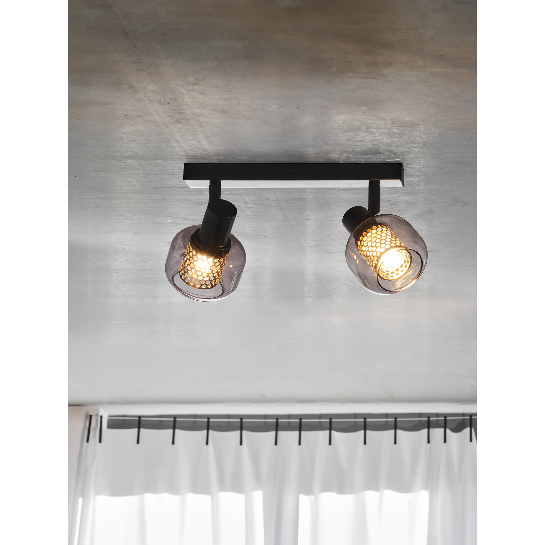Zwei moderne schwarze Deckenstrahler mit Rauchglas und Wabenmuster auf Betonhintergrund.