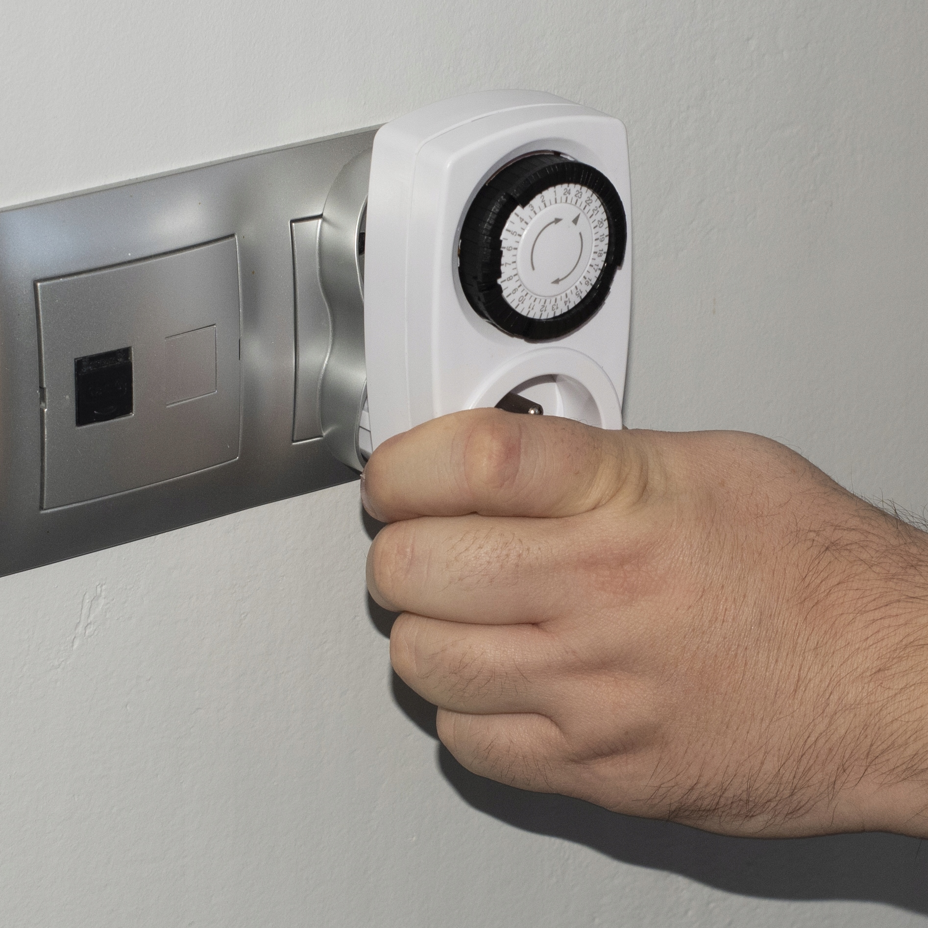 Dłoń wkłada biały zegar do gniazdka ściennego.