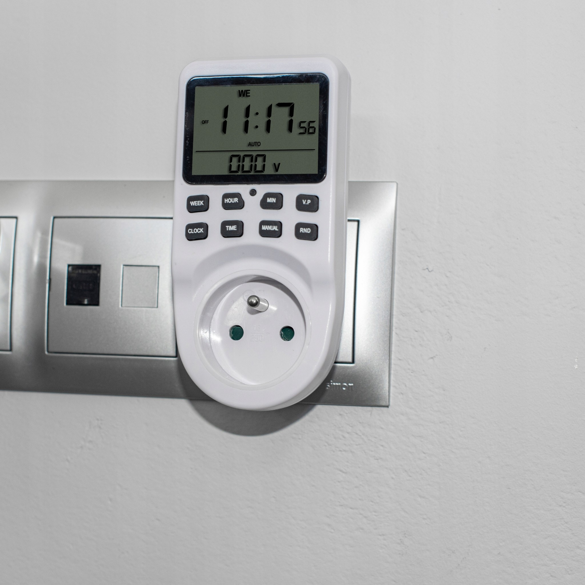 Biały cyfrowy programator czasowy z ekranem LCD podłączony do gniazdka ściennego.