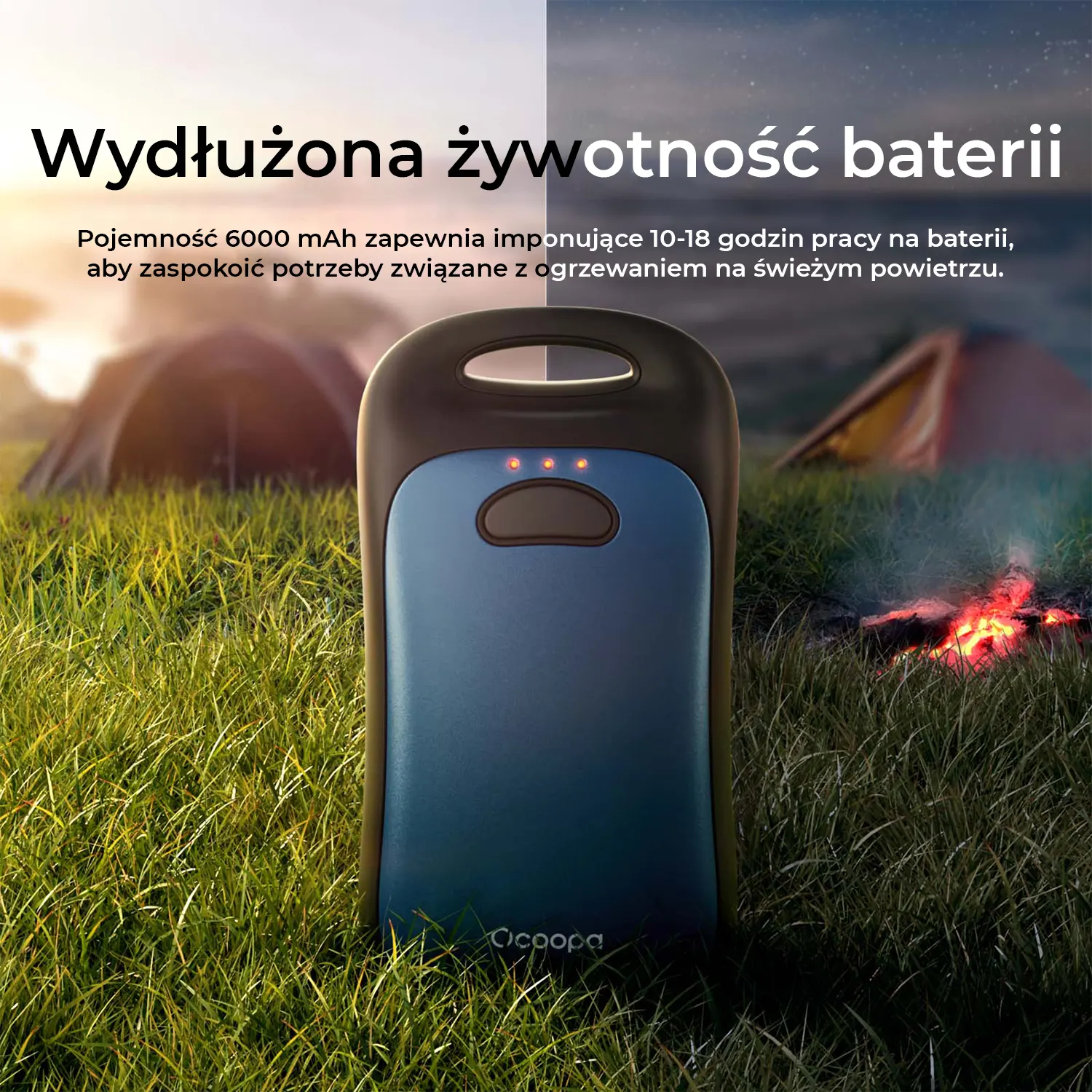 Niebieski power bank na trawie przed namiotami i ogniskiem.