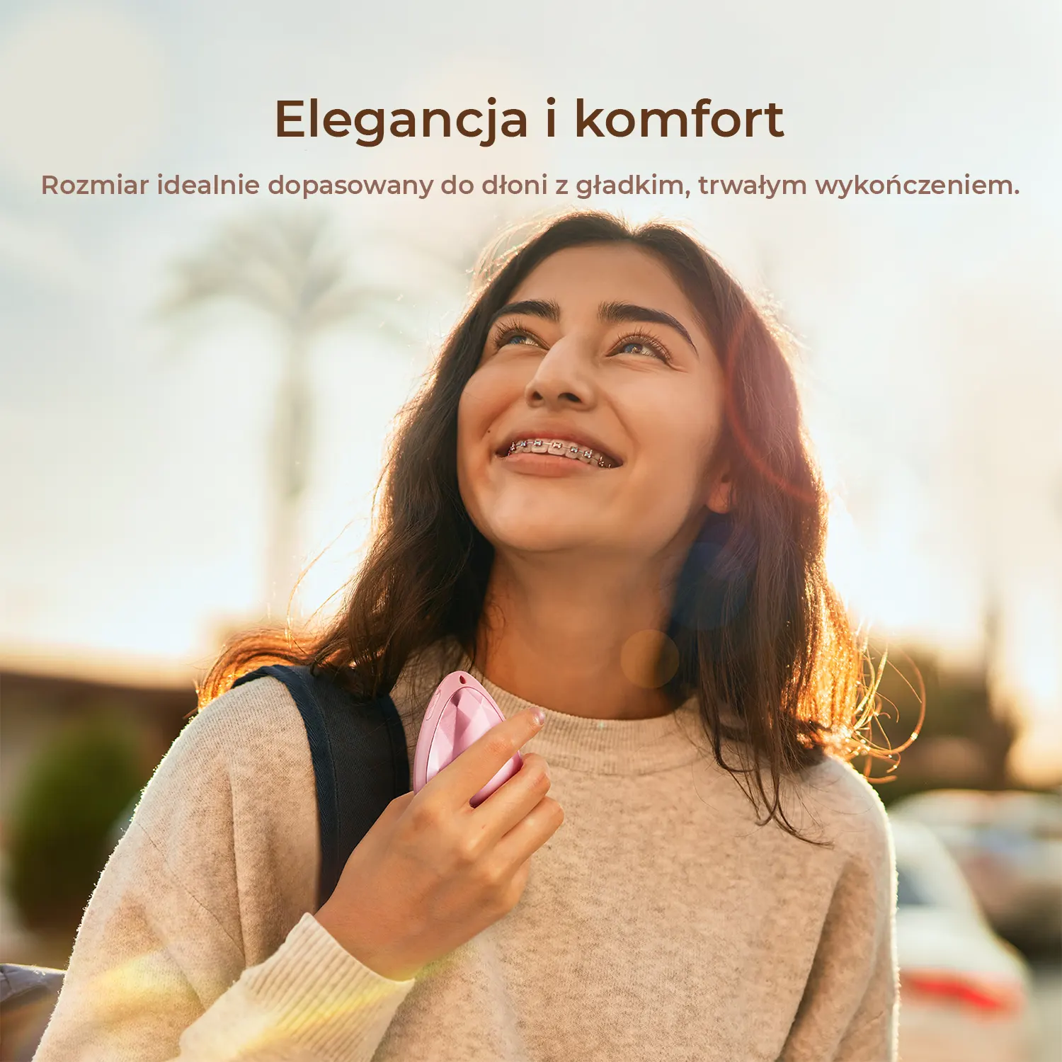 Młoda kobieta z aparatem na zębach trzyma różowe urządzenie na zewnątrz.