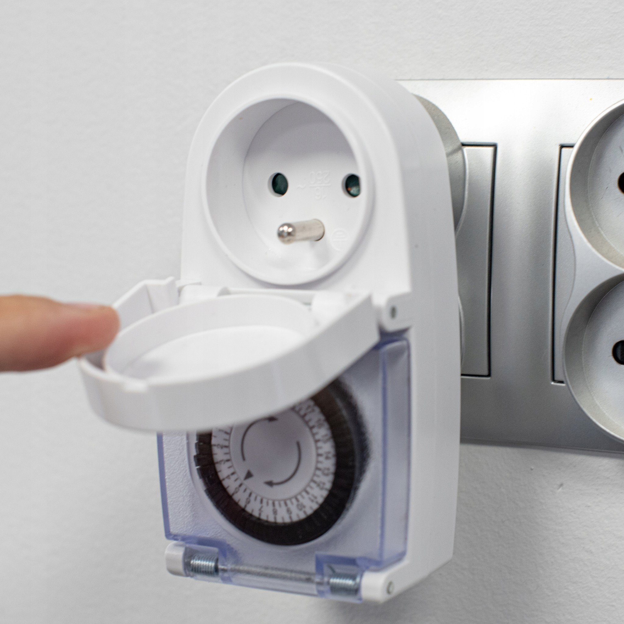 Palec otwiera pokrywę białego programatora podłączonego do gniazdka elektrycznego.