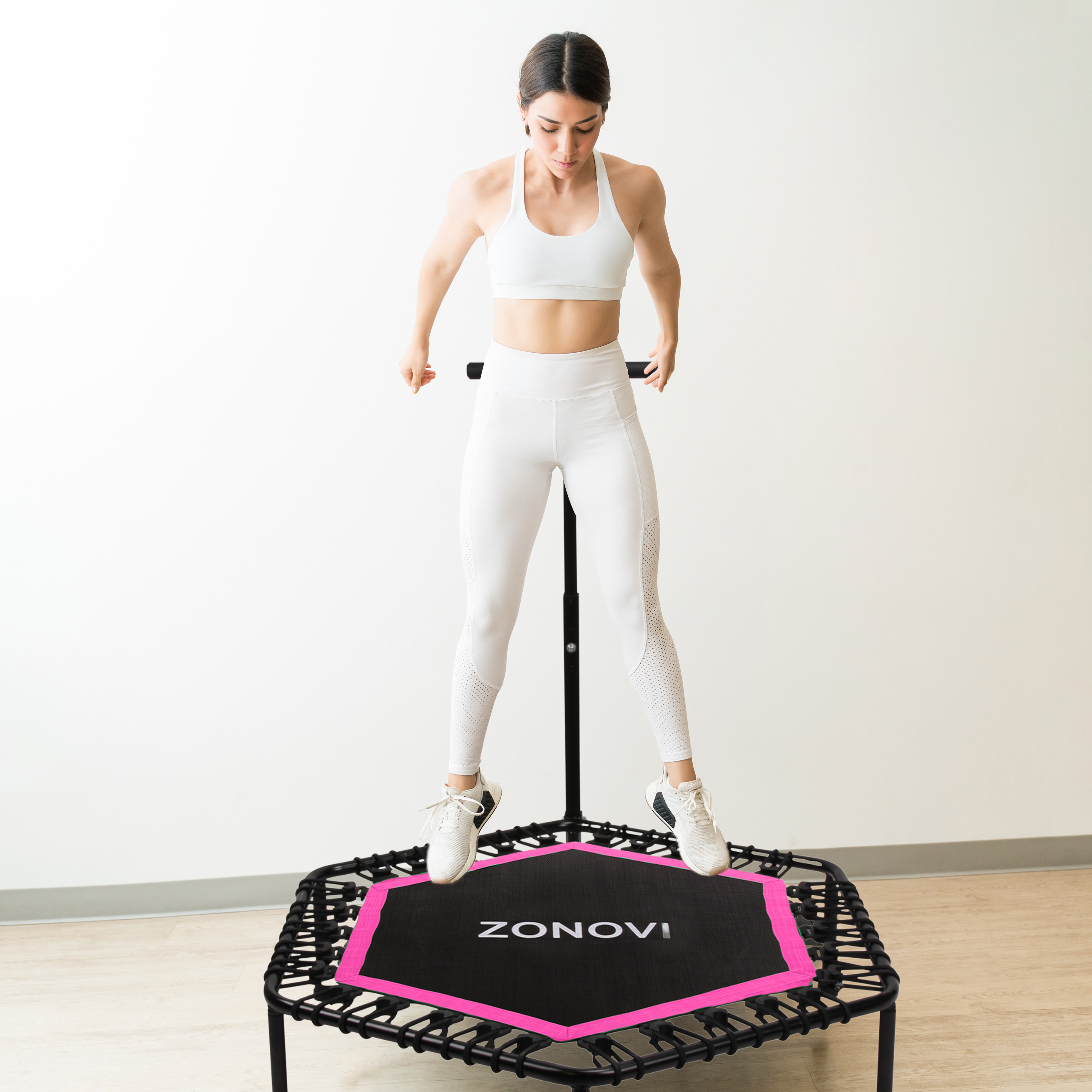 Een vrouw in witte sportkleding springt op een zwart trampoline met roze accenten.