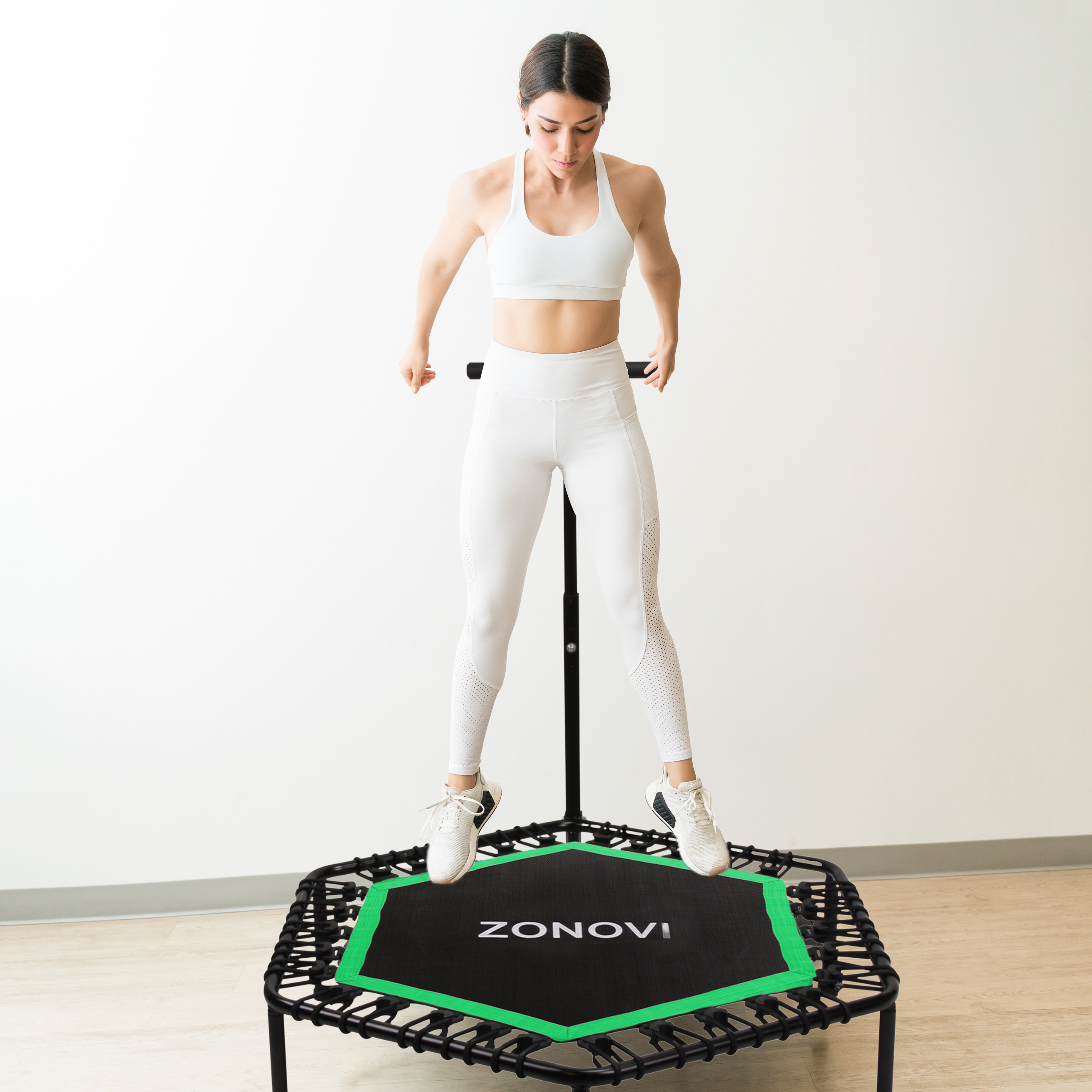 Vrouw in witte sportkleding springt op een zwart trampoline met groene rand.