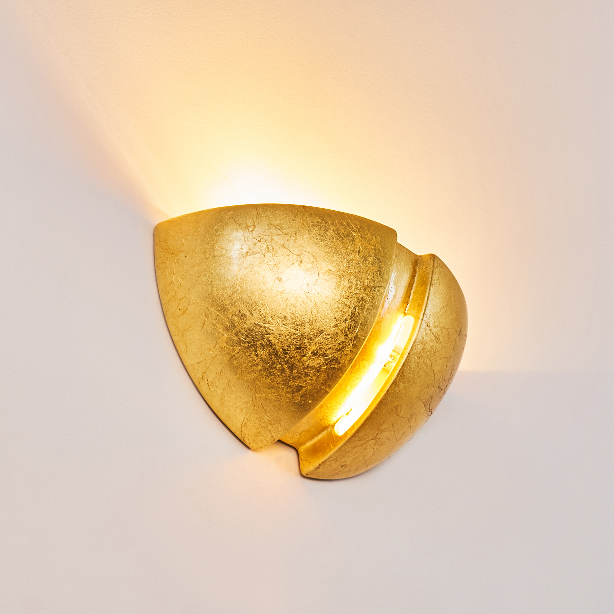 Goldene Wandleuchte mit beleuchtetem Stab und Lichtreflexionen an der Wand.