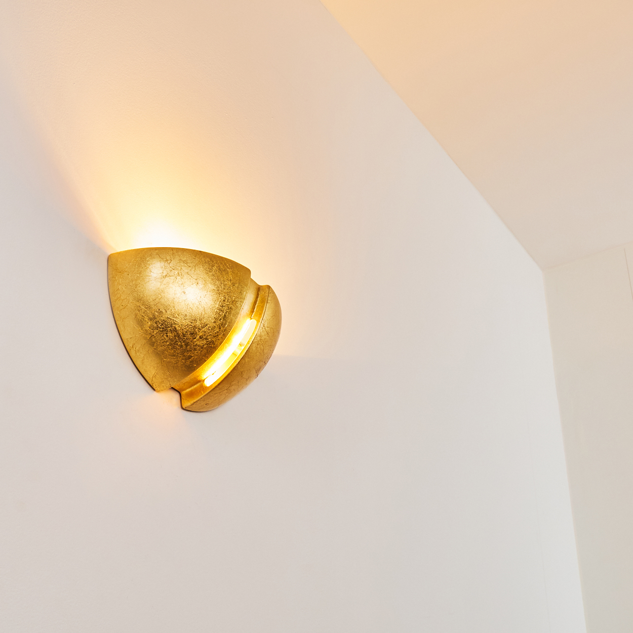 Goldene Wandleuchte beleuchtet weiße Wand mit warmem Licht.