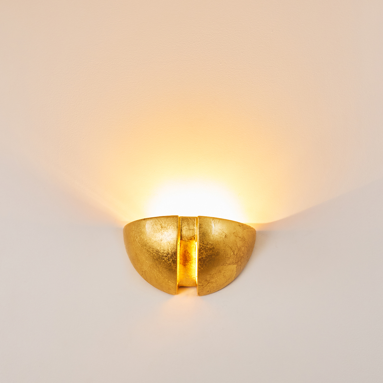 Eine goldene Wandleuchte mit texturierter Oberfläche wirft warmes Licht an die Wand.