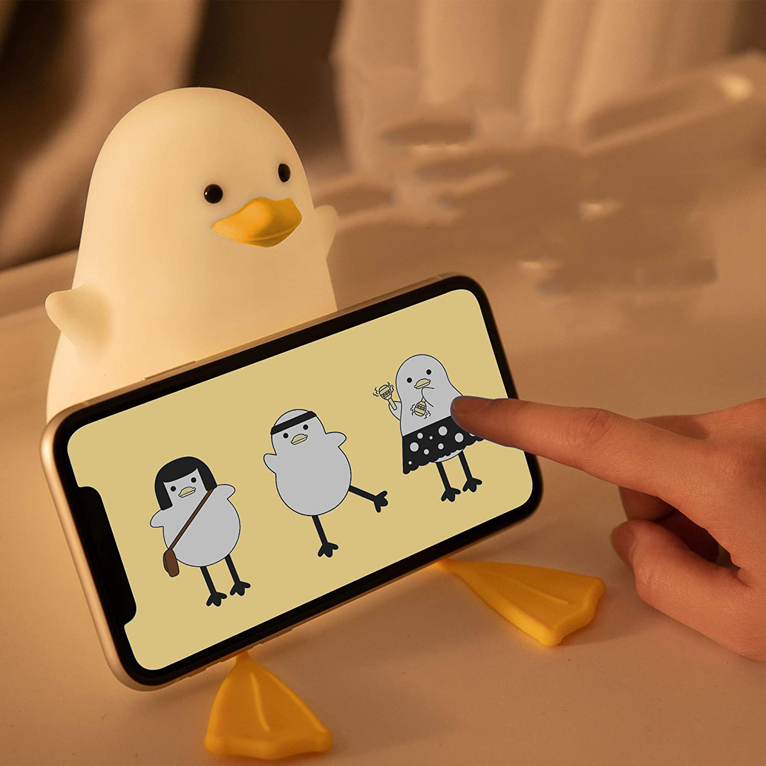 Eine leuchtende weiße Entenlampe neben einem Smartphone mit Cartoon-Vögeln.