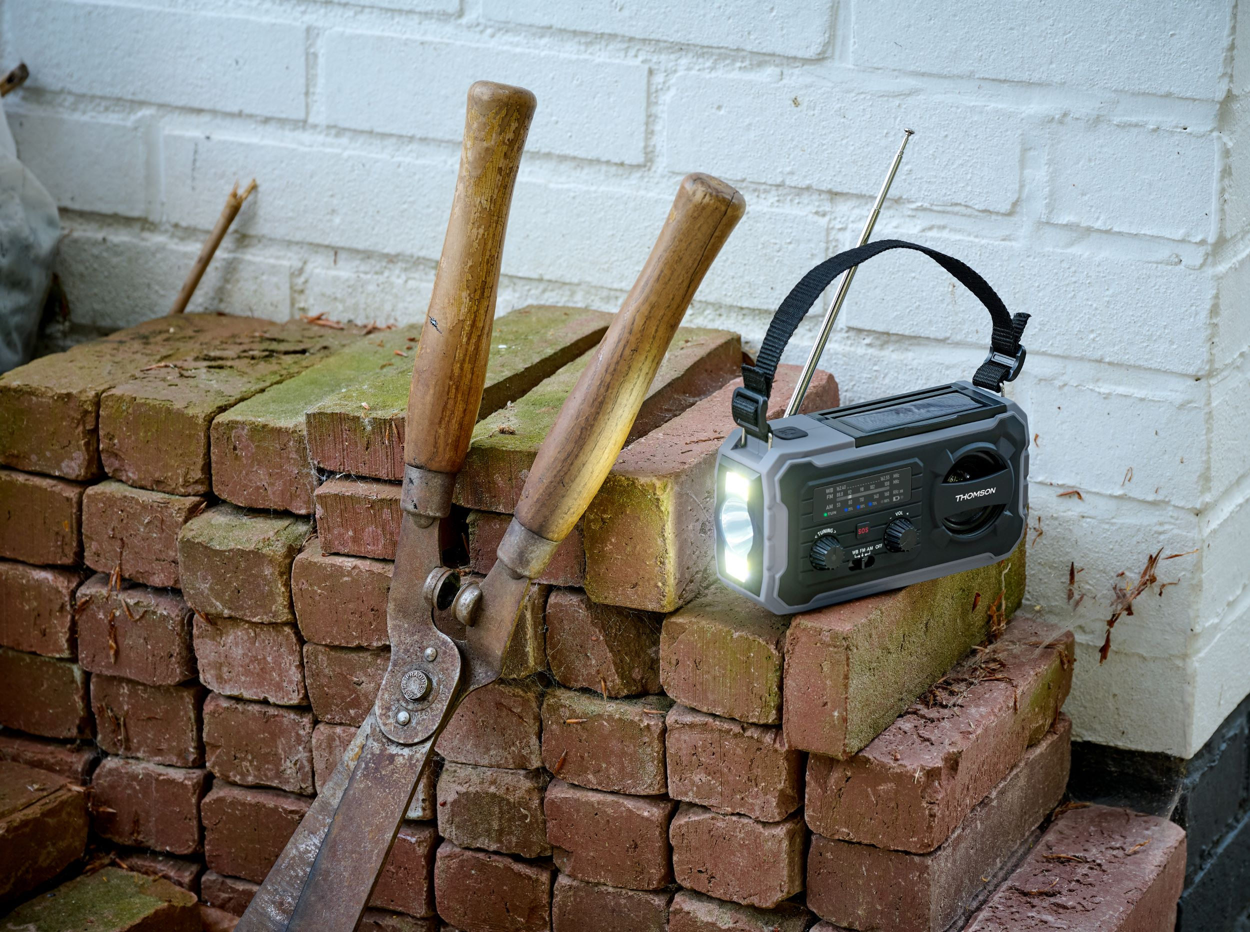 Radio z latarką i sekator na cegłach.