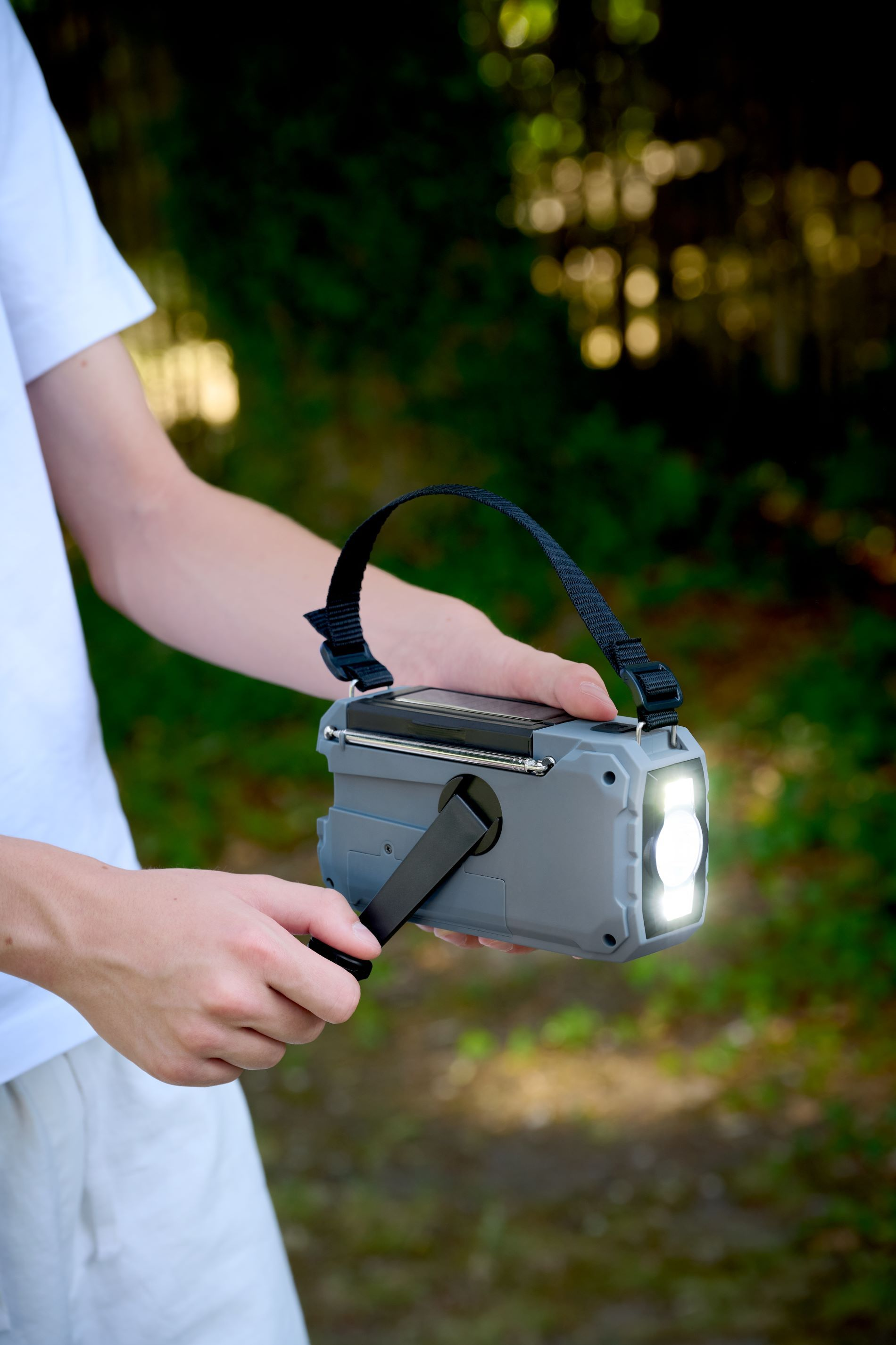 Szare radio awaryjne z korbą, panelem słonecznym i światłem w dłoni osoby.