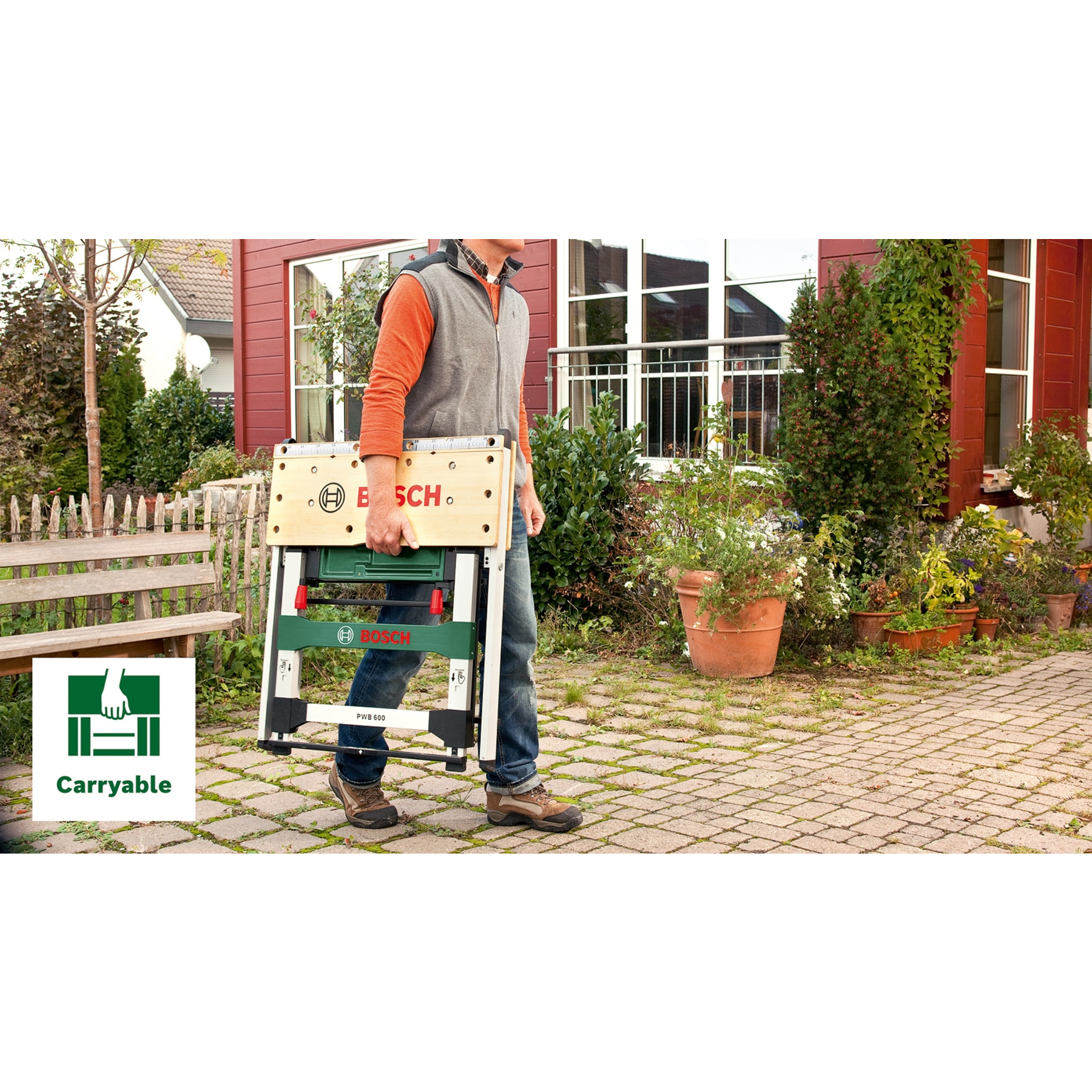 Ein Mann trägt einen zusammenklappbaren Werkzeugtisch von Bosch durch einen Garten.