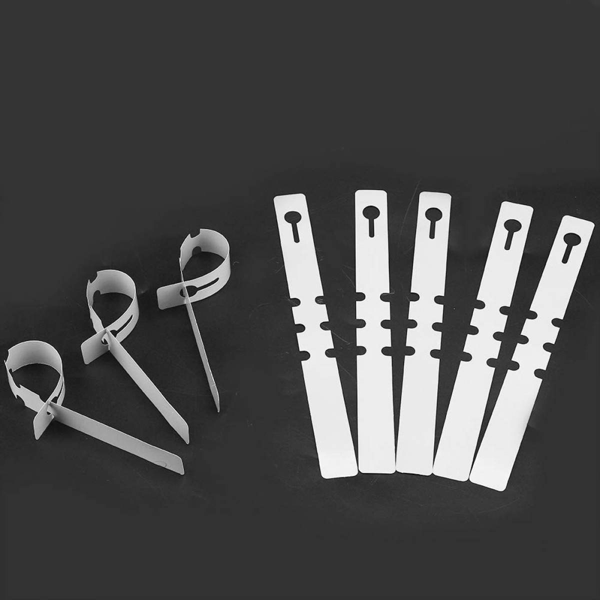 Drei weiße Kabelbinder mit Schlaufen und fünf weiße Pflanzenclips mit Loch.