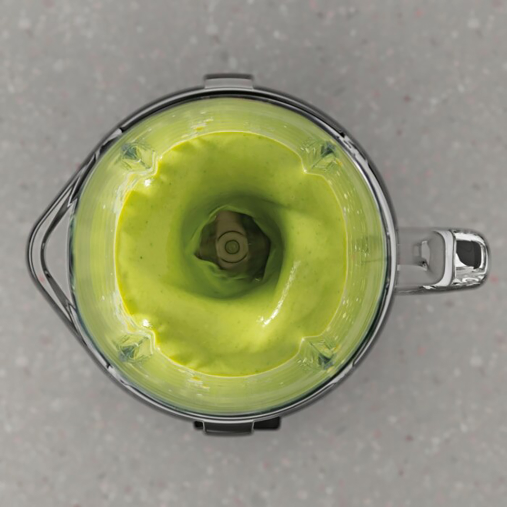 Purea di frullato verde vortica in un frullatore su un piano di lavoro in pietra.