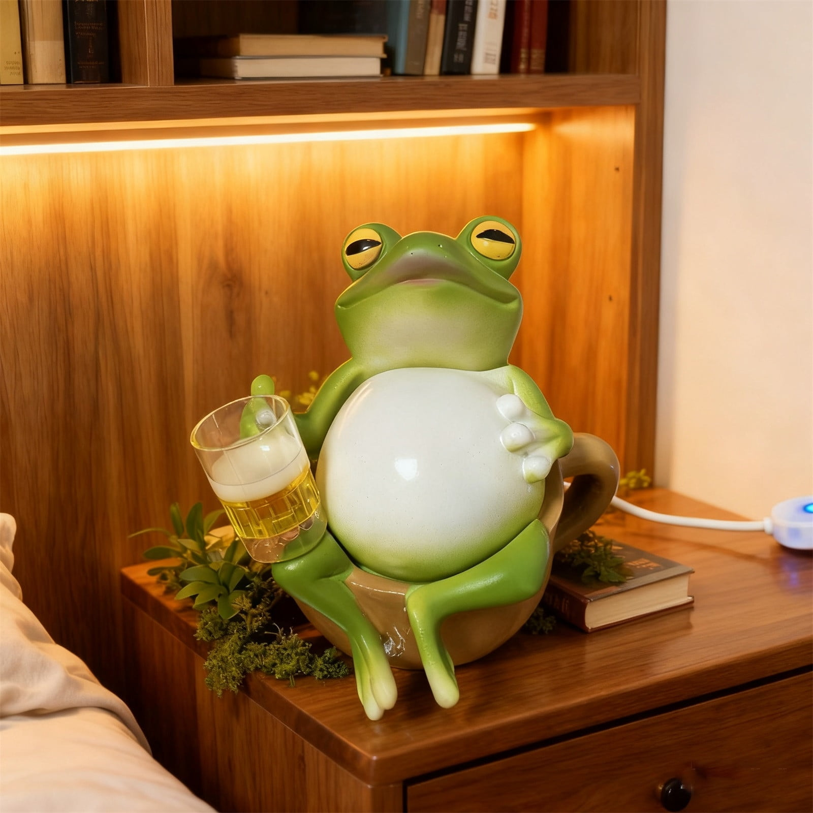Eine grüne Froschfigur sitzt in einer Tasse und hält ein Glas Bier.