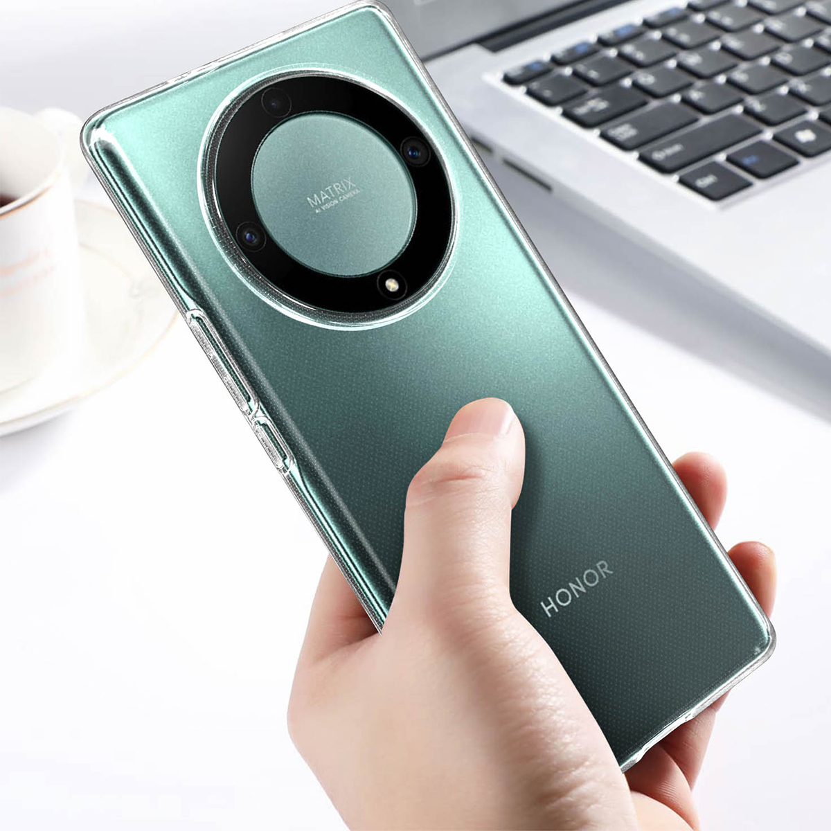 Una mano tiene uno smartphone verde con fotocamera circolare. Un laptop sullo sfondo.
