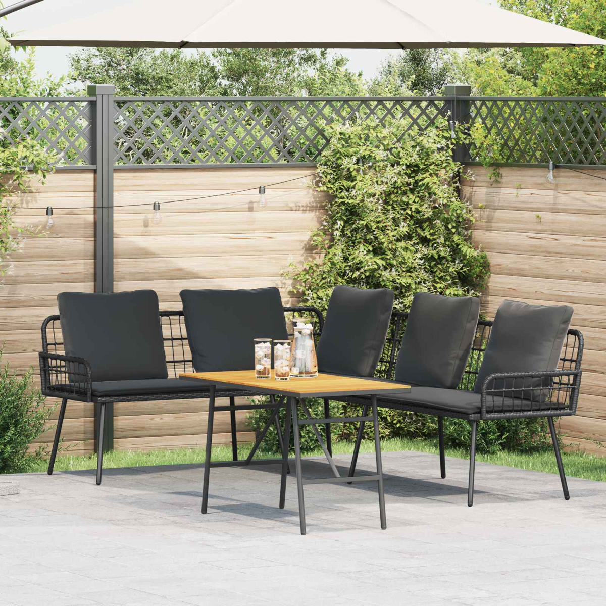 Gartenlounge mit vier schwarzen Kissen, Holztisch und Gläsern.