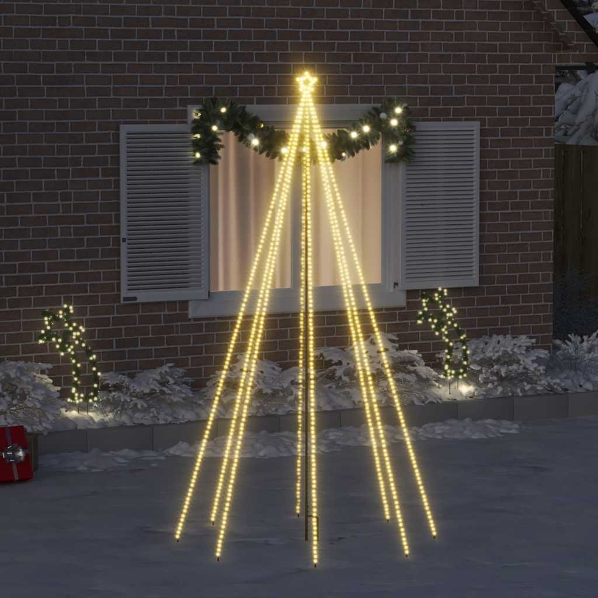 Ein beleuchteter Weihnachtsbaum mit gelben Lichtern vor einem Ziegelhaus mit Fenster.