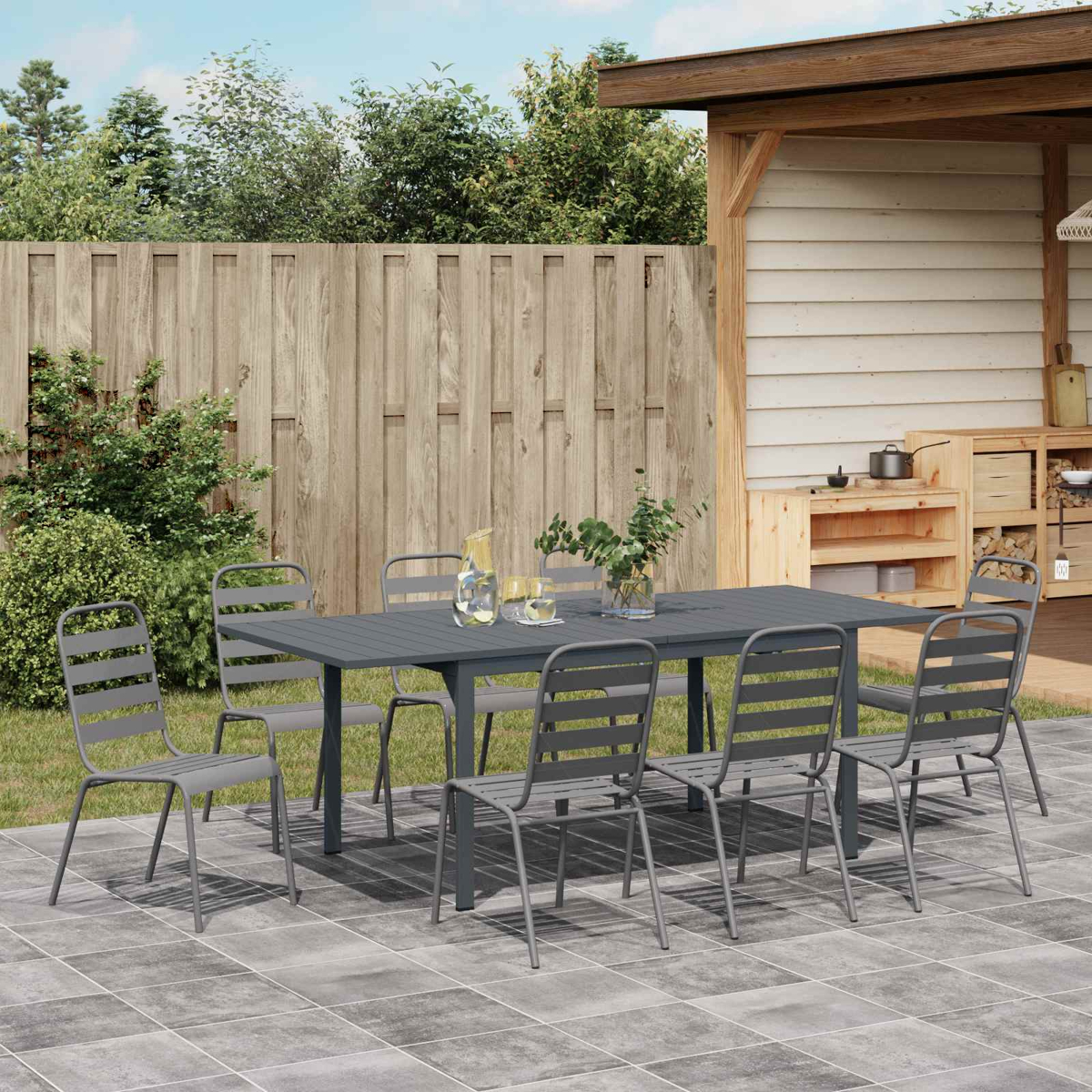 Ein grauer Gartentisch mit acht Stühlen auf einer gepflasterten Terrasse.