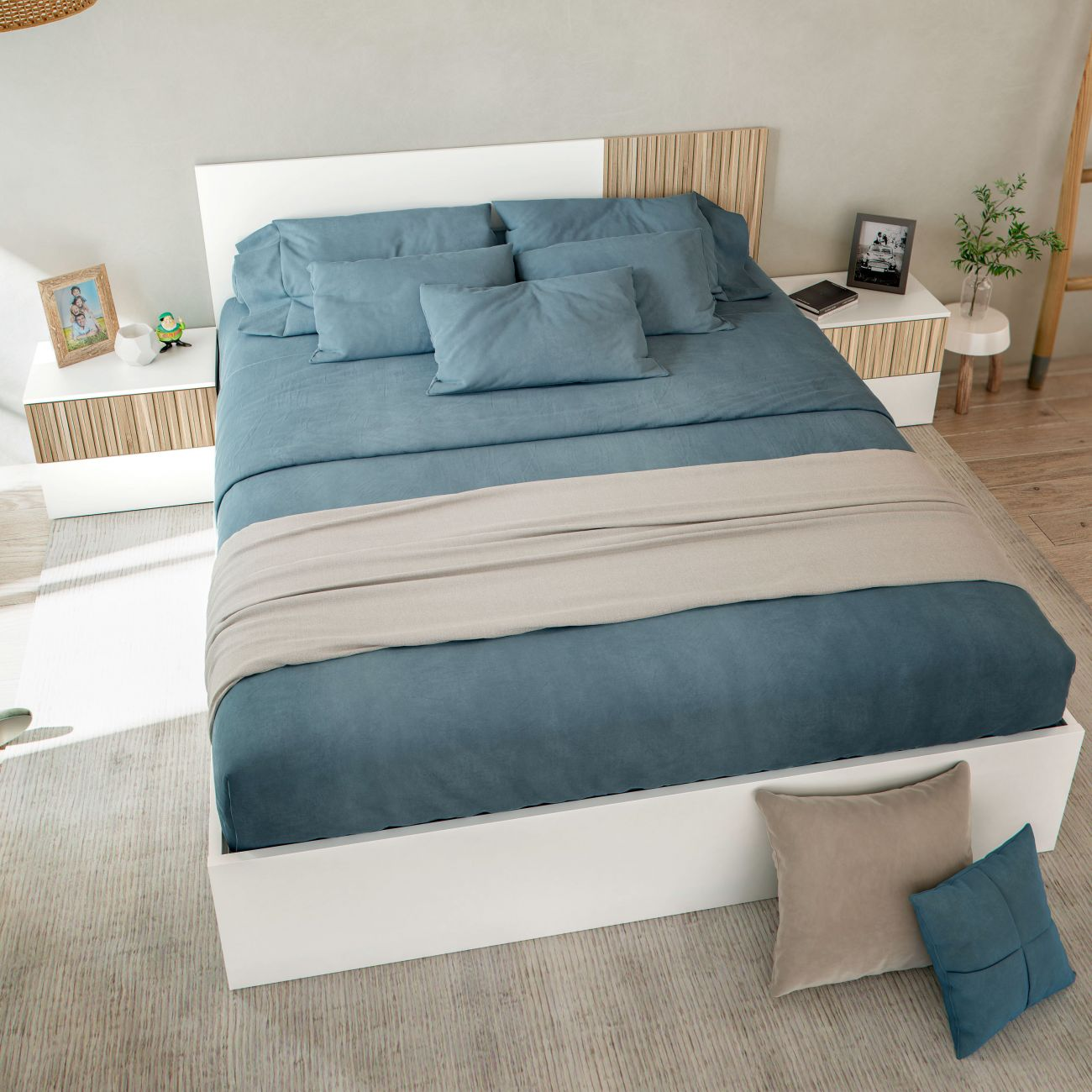 Una cama azul con cojines y manta, mesitas de noche con marcos y plantas.