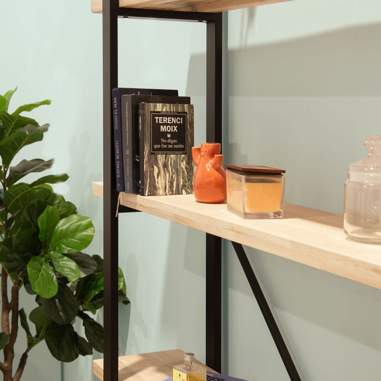 Una estantería con libros, jarrón naranja, vela y planta.