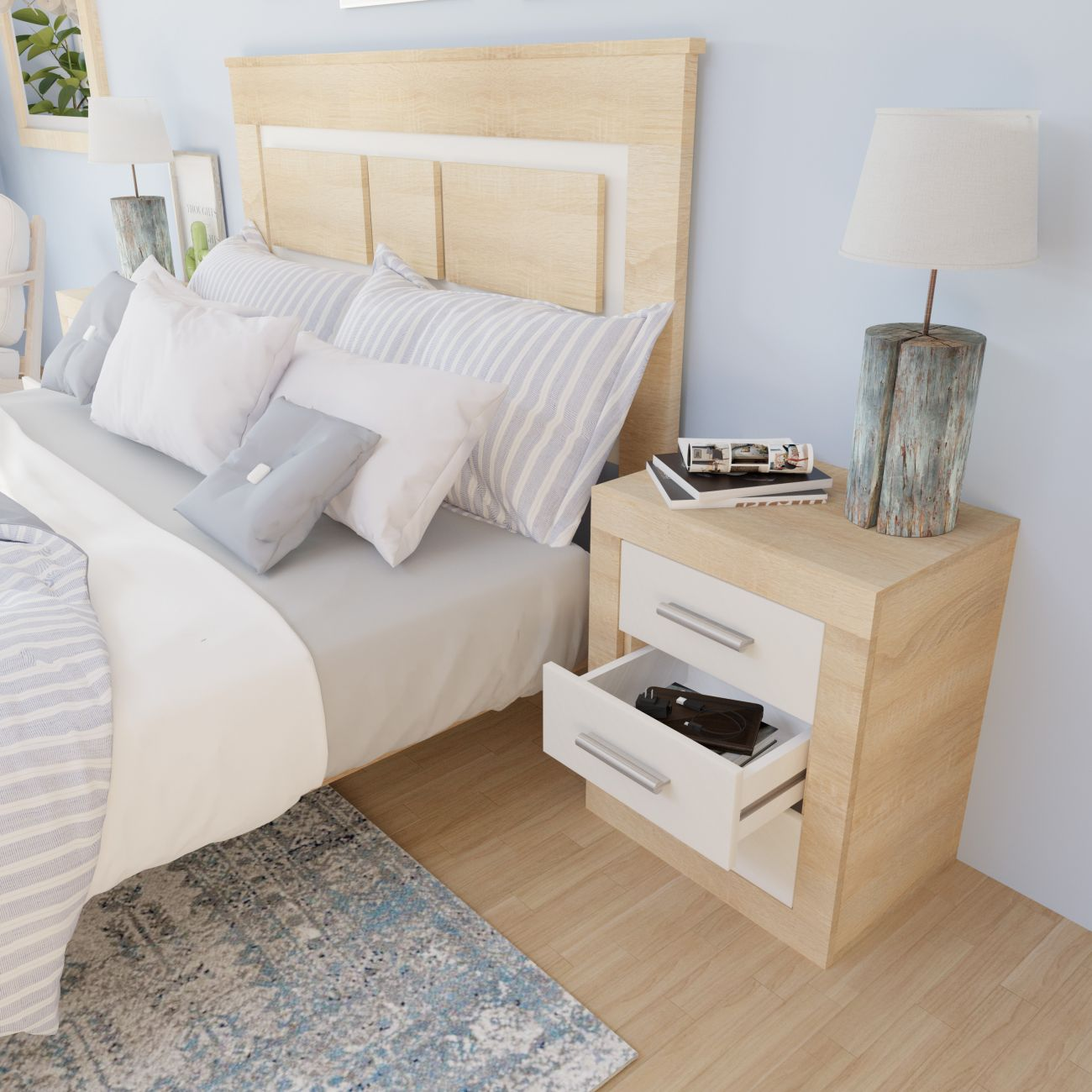 Cabecero de madera clara sobre cama con almohadas blancas y rayadas. Mesita de noche con lámpara, libros y cajón abierto.