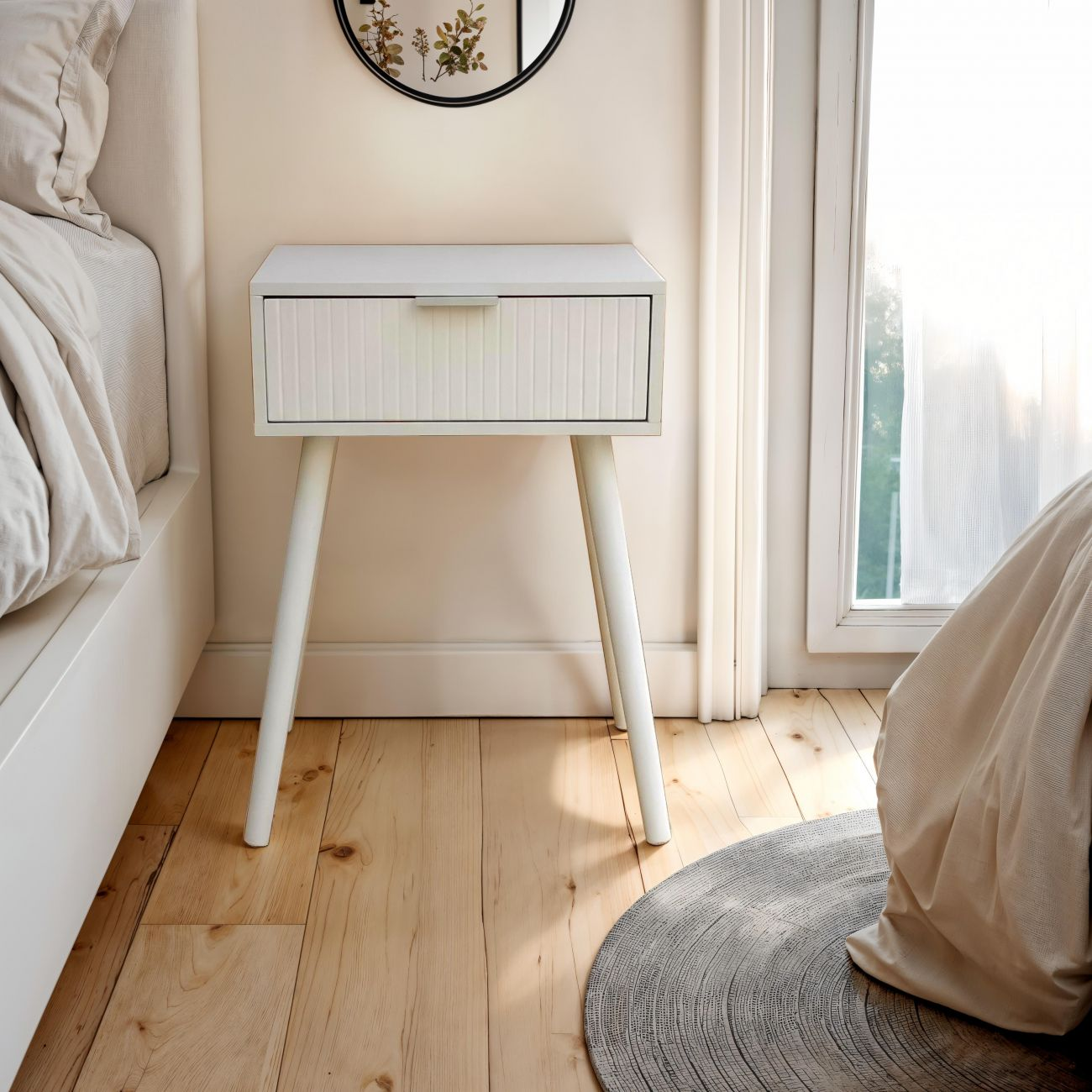 Una mesita de noche blanca con cajón acanalado junto a una cama.