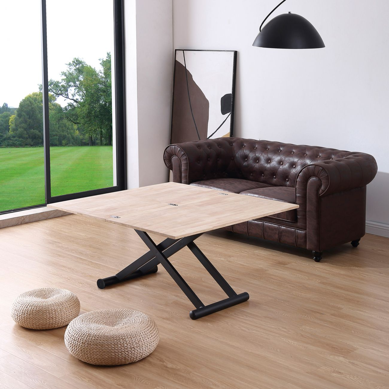 Una mesa de madera con base de tijera negra está delante de un sofá de cuero marrón.