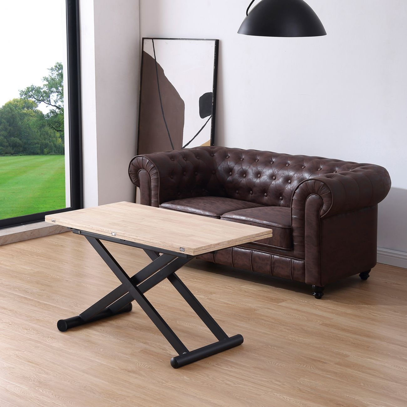 Una mesa de madera clara con base de tijera negra está frente a un sofá de cuero marrón.