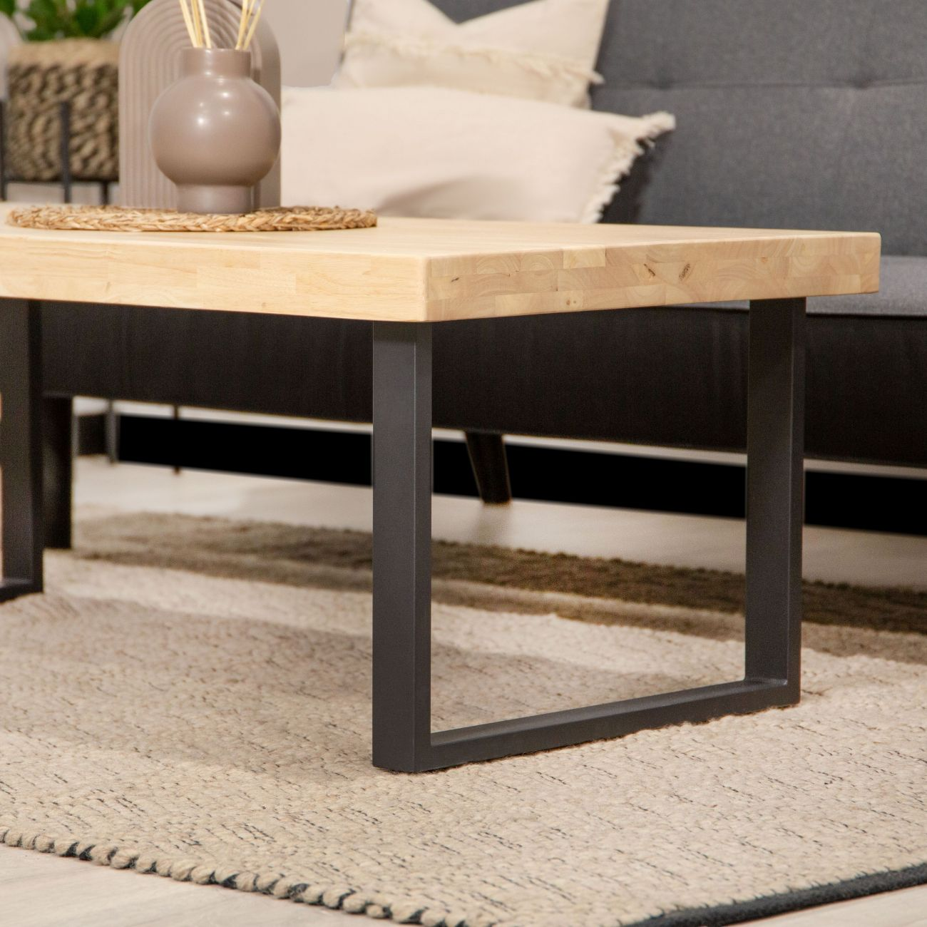 Mesa de centro de madera con patas de metal sobre alfombra frente a sofá.