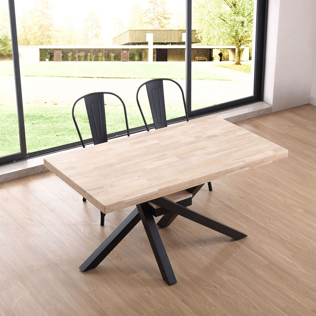 Mesa de madera con patas de metal y dos sillas negras frente a una ventana grande.