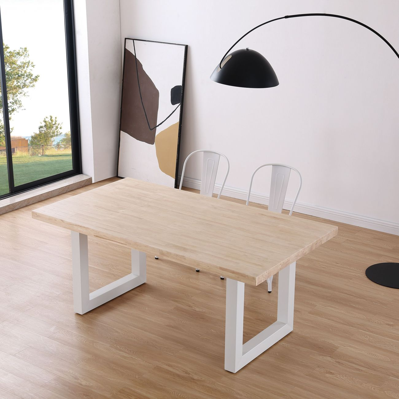 Una mesa de madera clara con patas blancas, dos sillas blancas y una gran lámpara de arco.