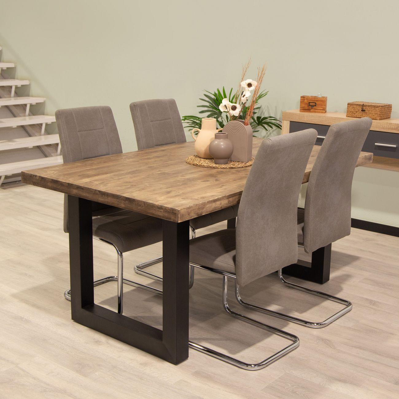 Mesa de madera con cuatro sillas grises, decorada con jarrones y plantas.